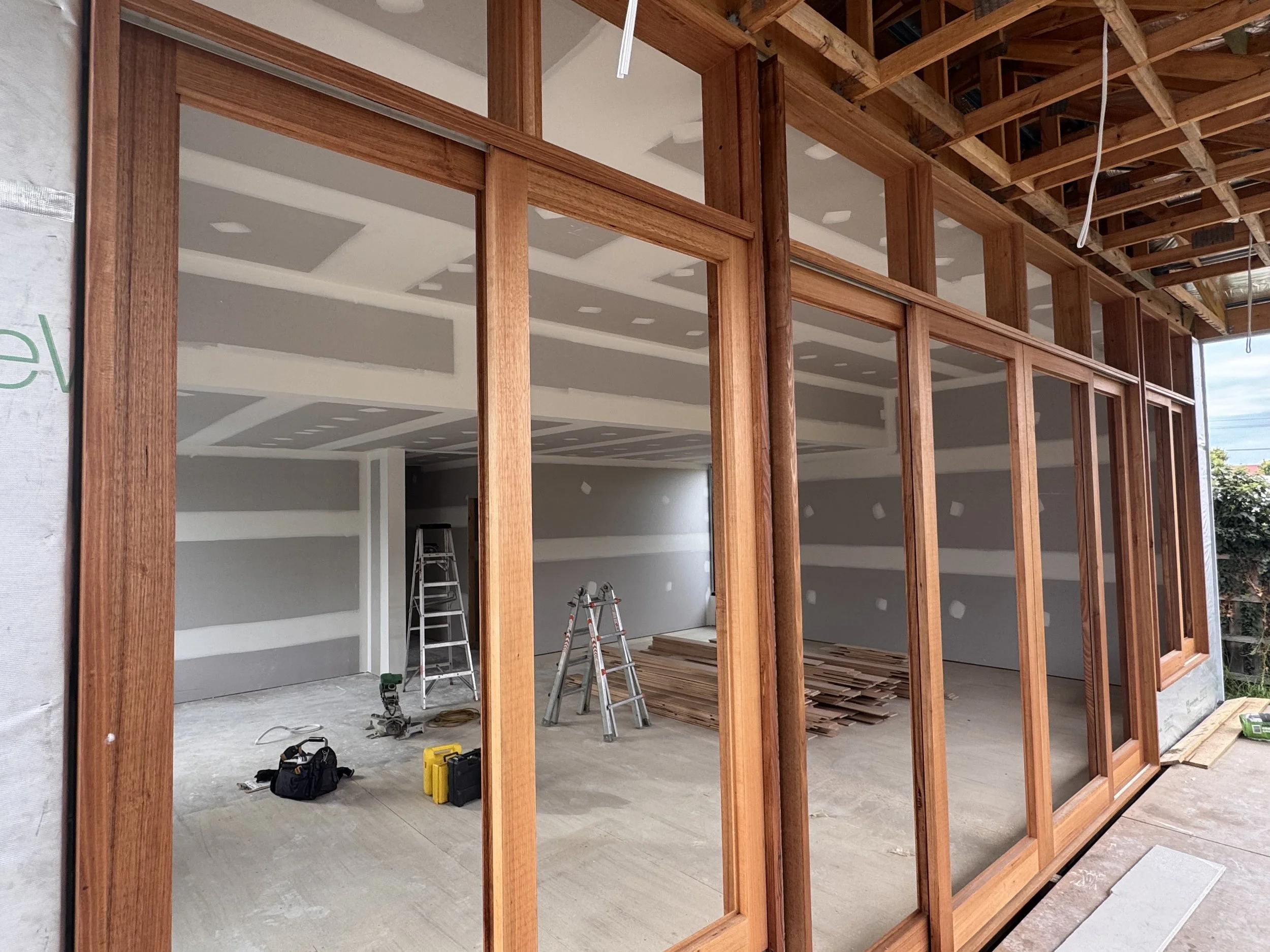Construction site showing a partially built interior with wooden framing, ladders, construction tools, and drywall installed on the walls.