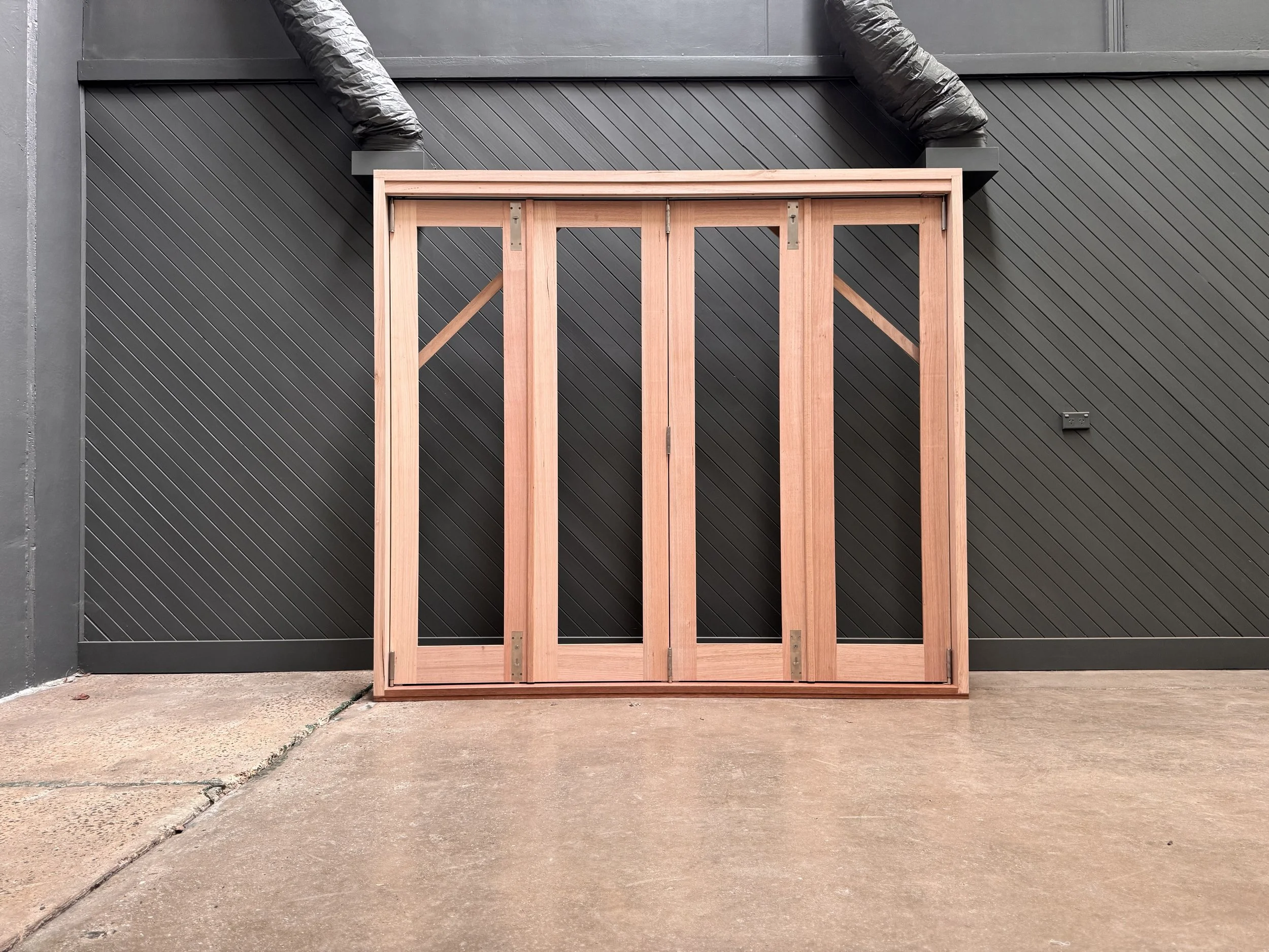 Wooden door frame leaning against a black wall with diagonal paneling and a black electrical outlet, on a concrete floor.
