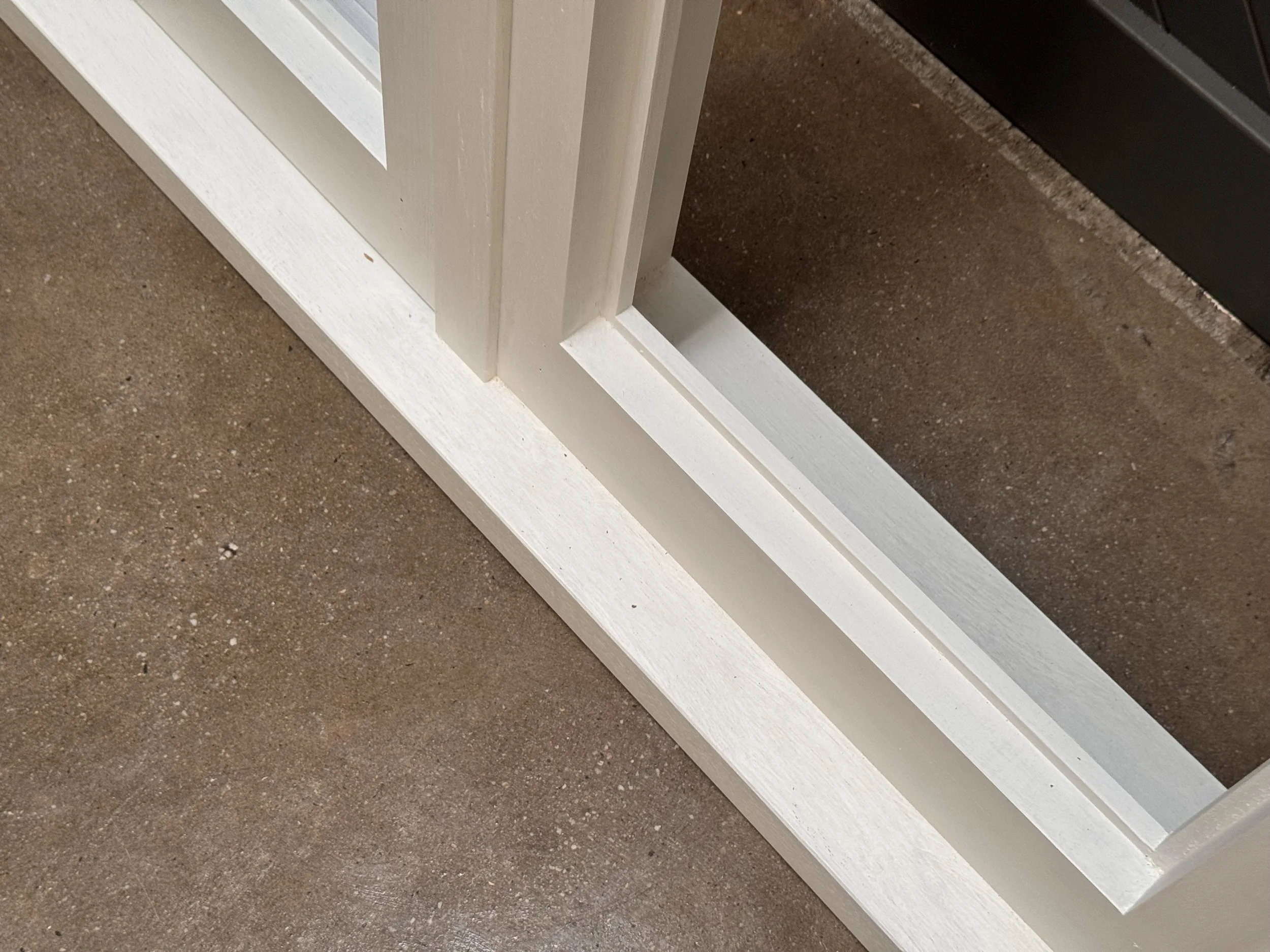 Close-up of white wooden window or door frame on brown concrete floor.