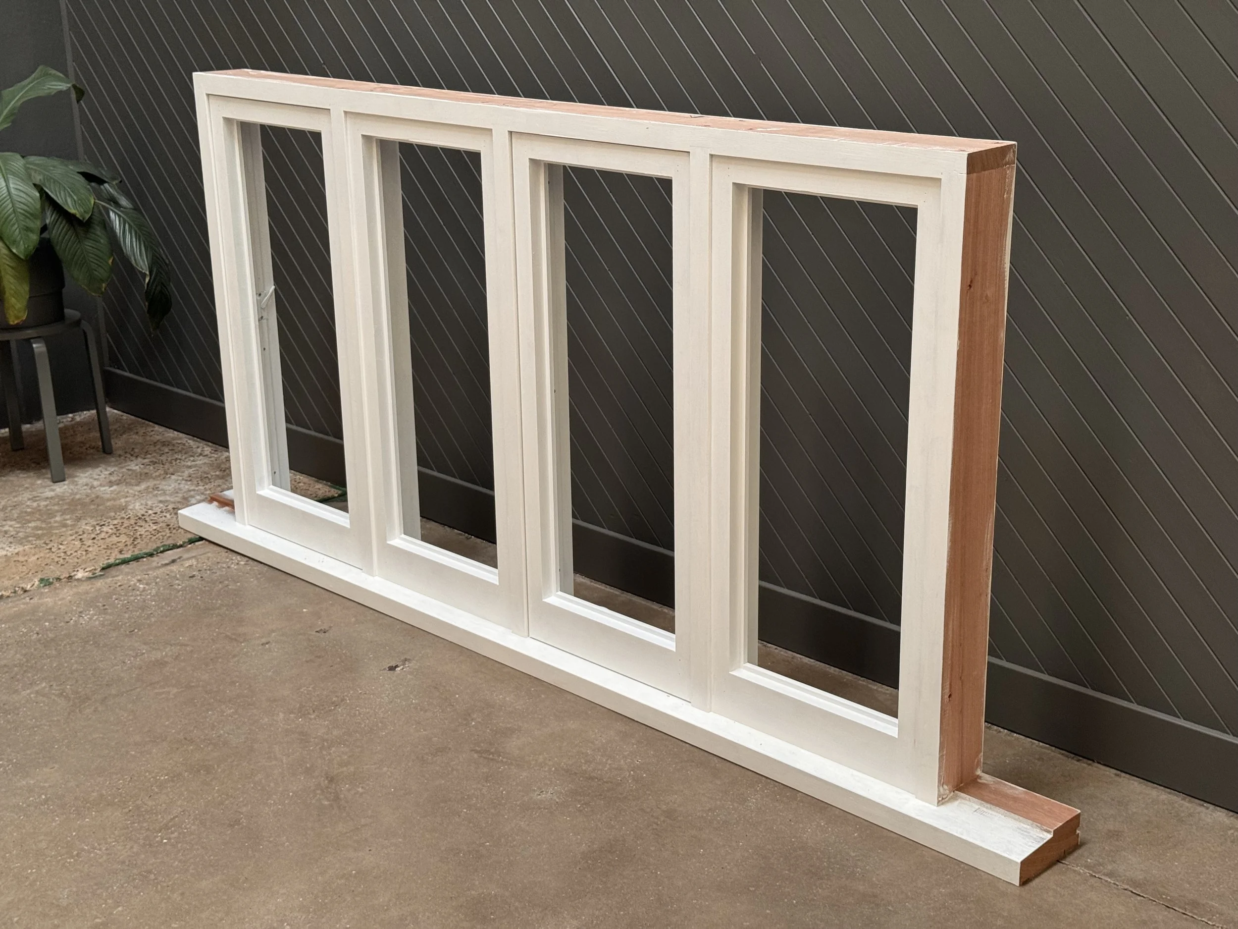 Unassembled wooden window frames leaning against a dark wall in a workshop or construction site.