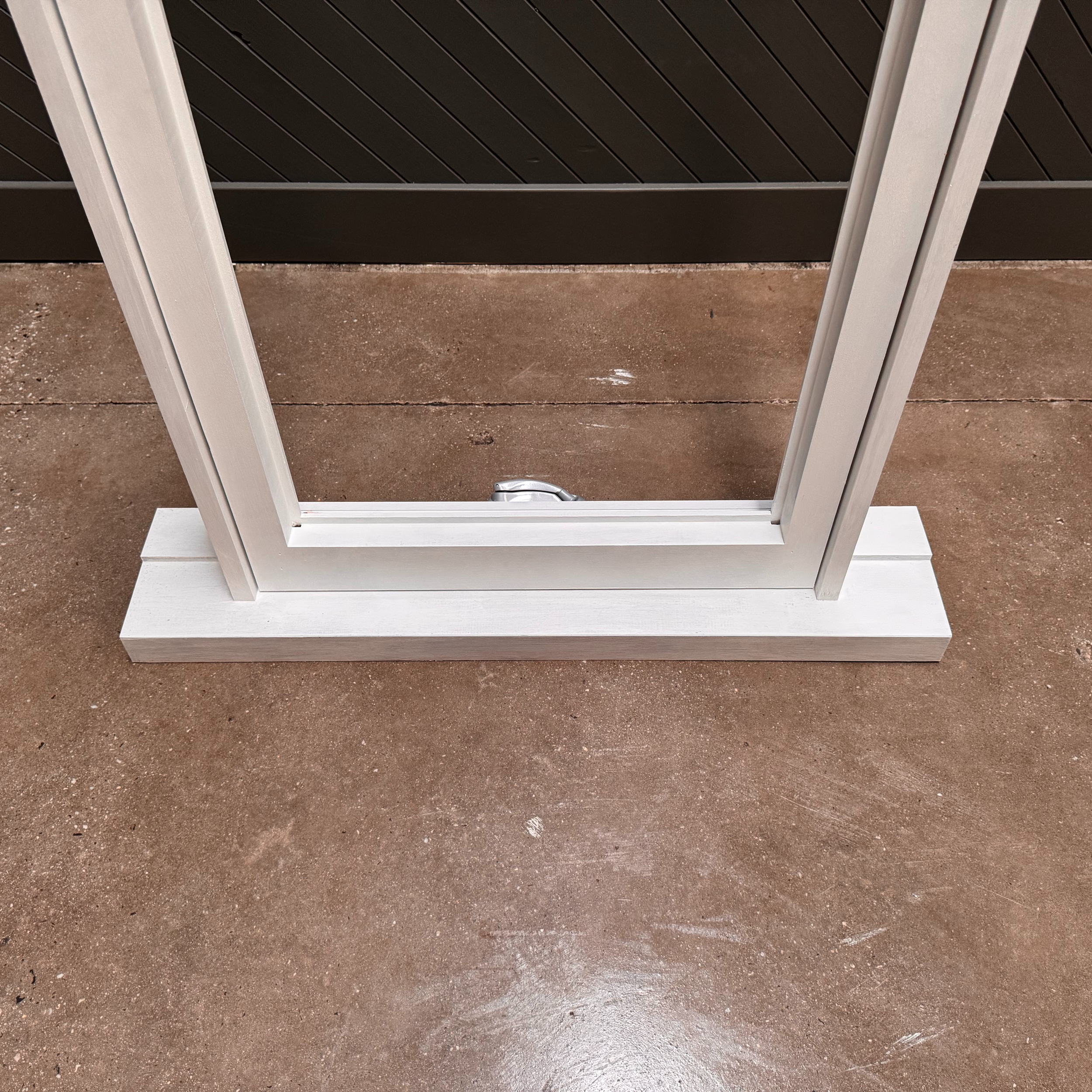 Close-up of a white standing picture frame on a brown concrete floor with a black fence in the background.