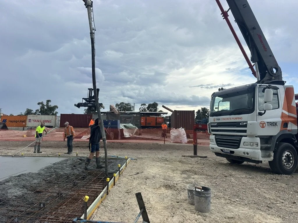 Construction workers pouring concrete on a building site with a concrete pump truck in the background and storm clouds overhead.