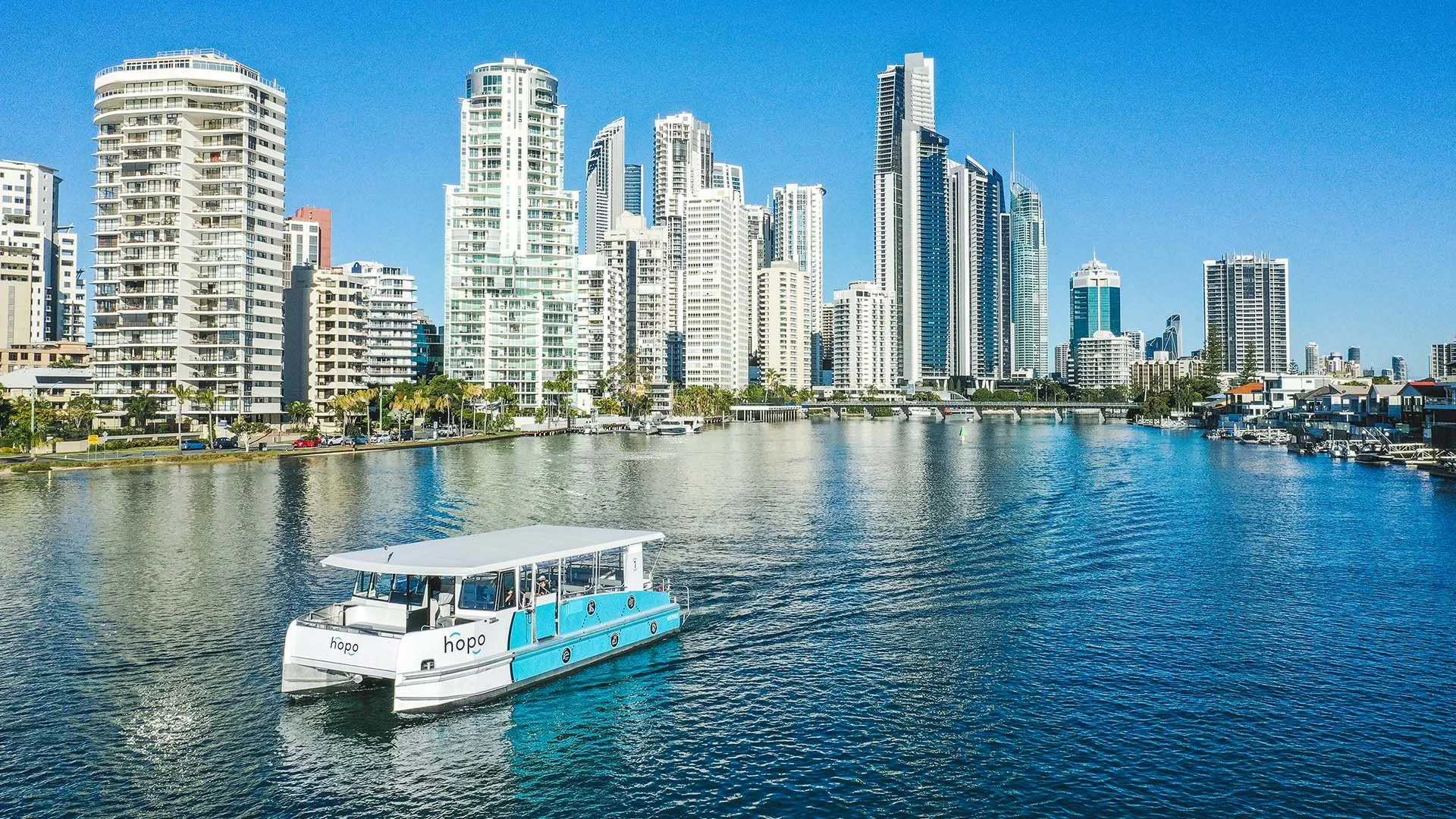 A boat named 'hope' on a body of water near a city skyline with tall modern buildings under a clear blue sky.
