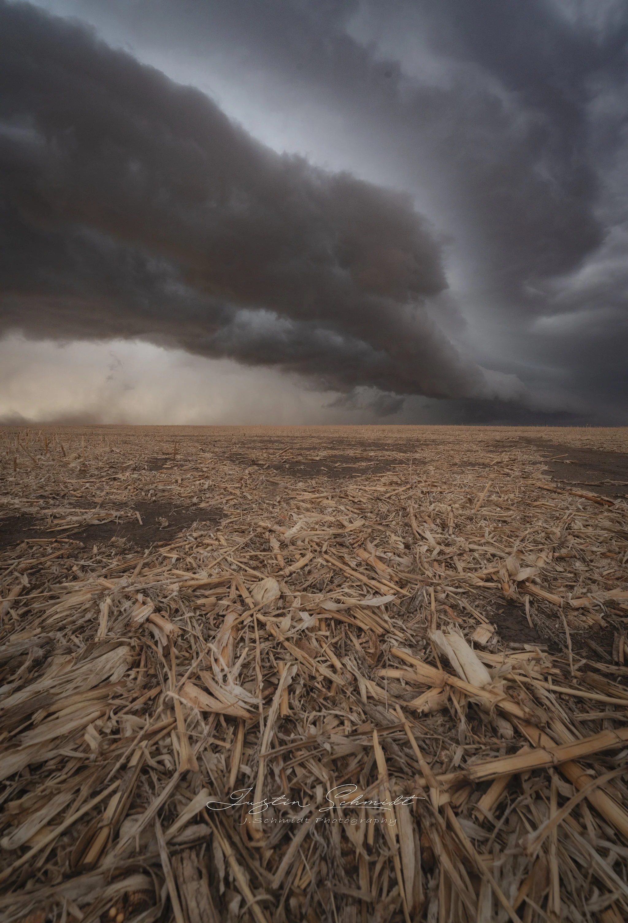 Dark storm clouds over a barren, harvested field of straw or corn stalks.