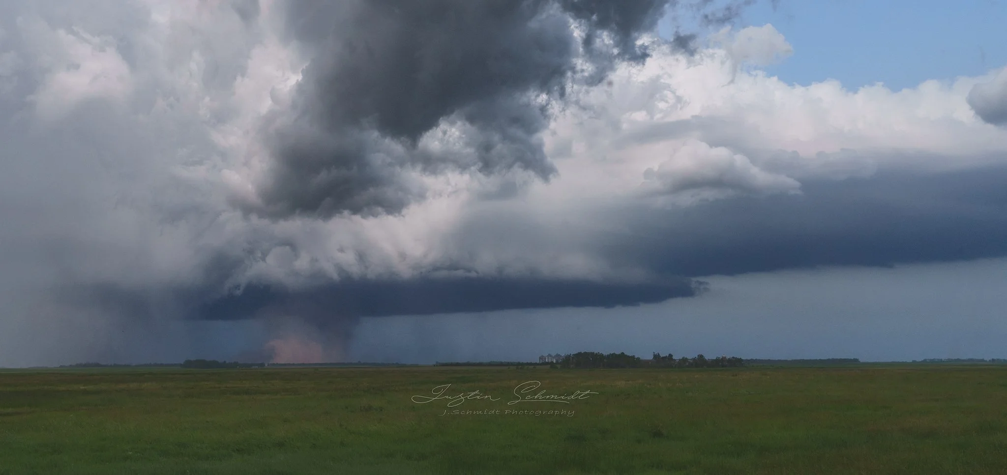 A tornado is forming on flat green grassland under dark, stormy clouds.