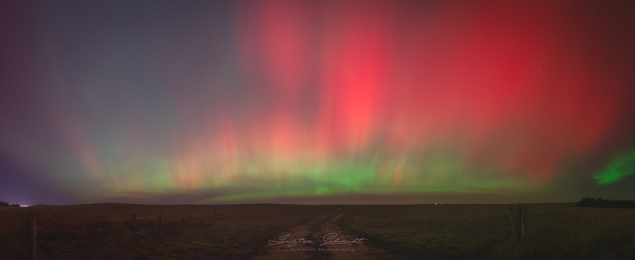 Nighttime landscape with colorful aurora borealis in the sky over open fields.