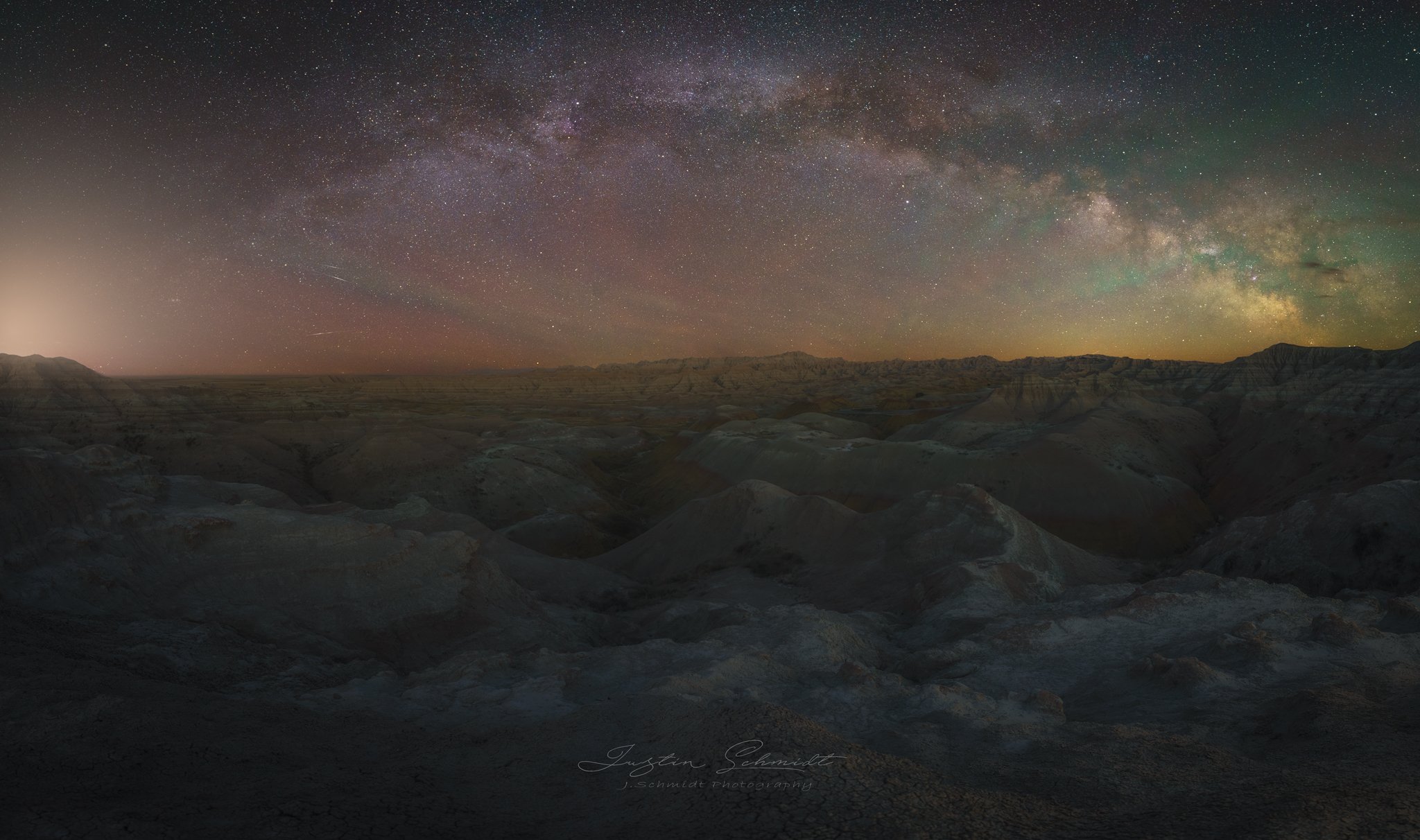 Night sky filled with stars and the Milky Way galaxy over rugged desert terrain at night.