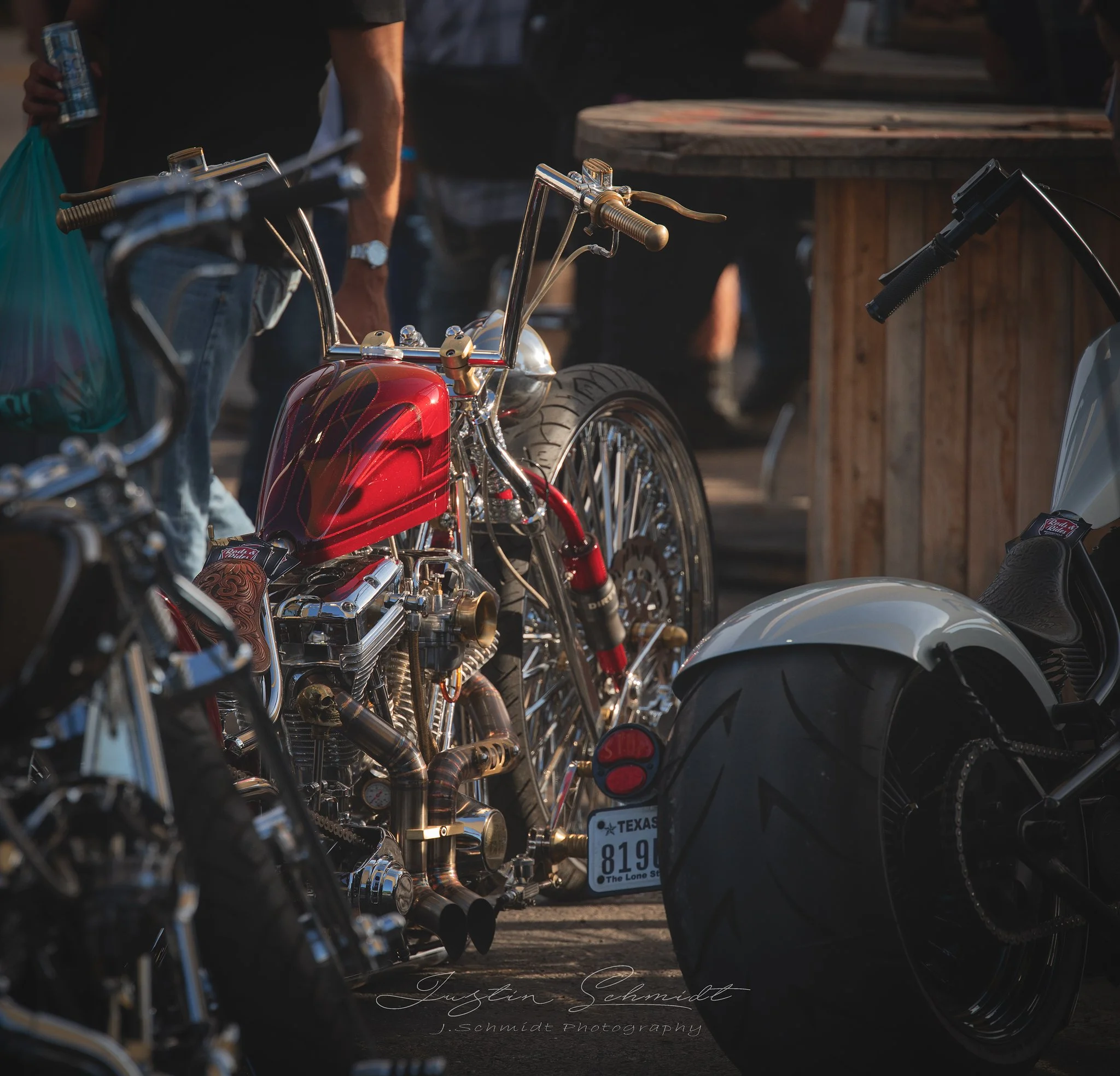 A custom vintage motorcycle with a red tank and chrome details parked next to a streamlined motorcycle with a white fender and large rear tire, outdoors during daytime.