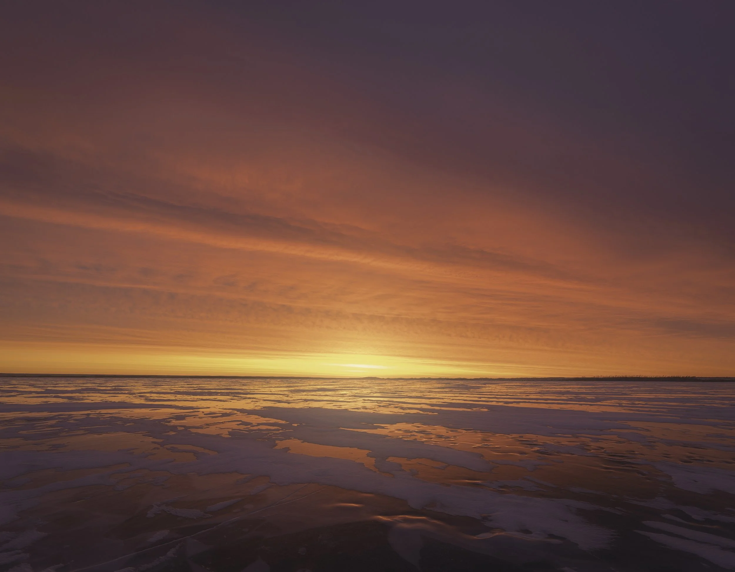 A vibrant sunset over a frozen body of water, with streaks of orange, pink, and purple in the sky.