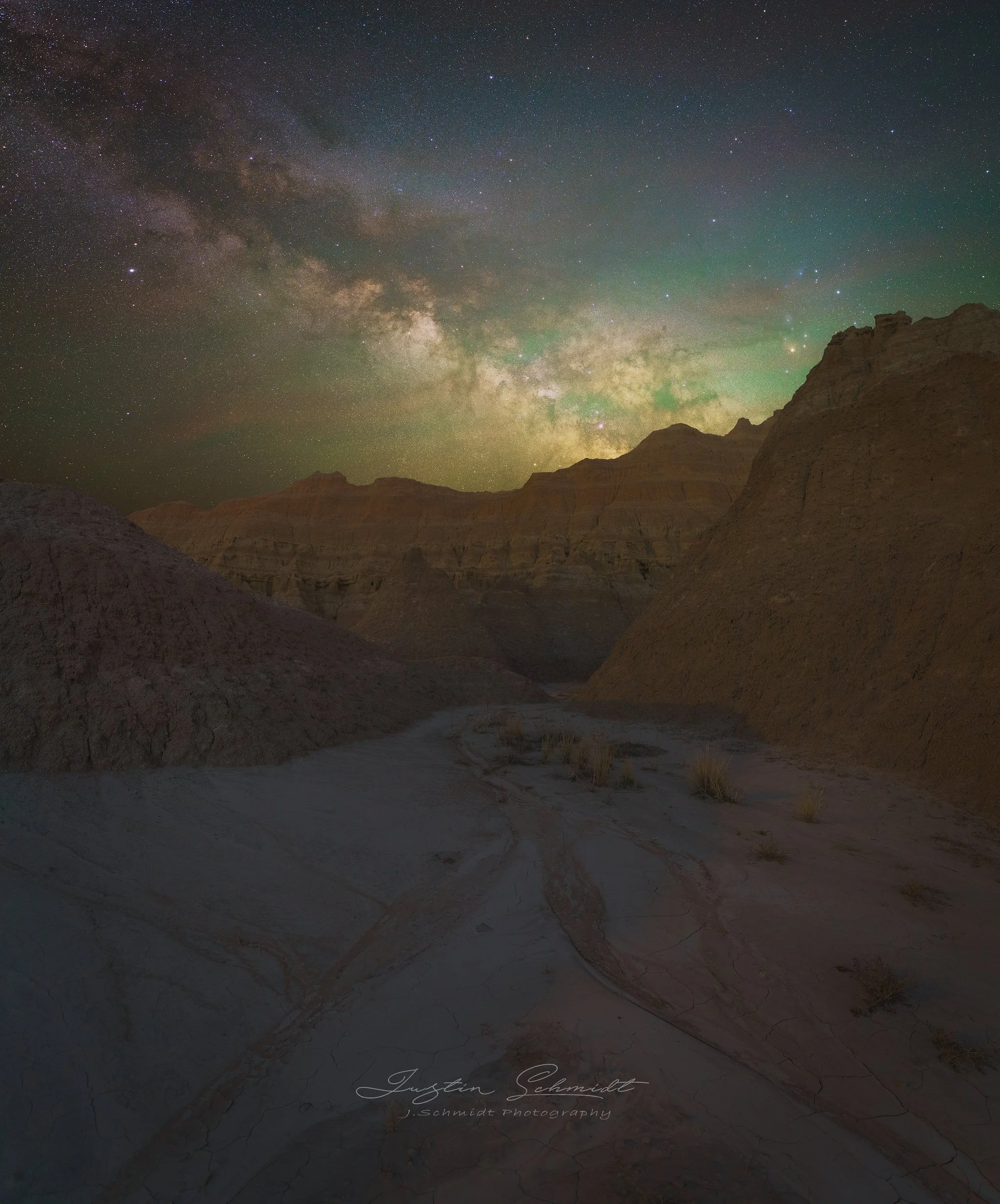Nighttime landscape of a canyon with rugged cliffs under a starry sky, featuring the Milky Way galaxy and luminous green aurora.
