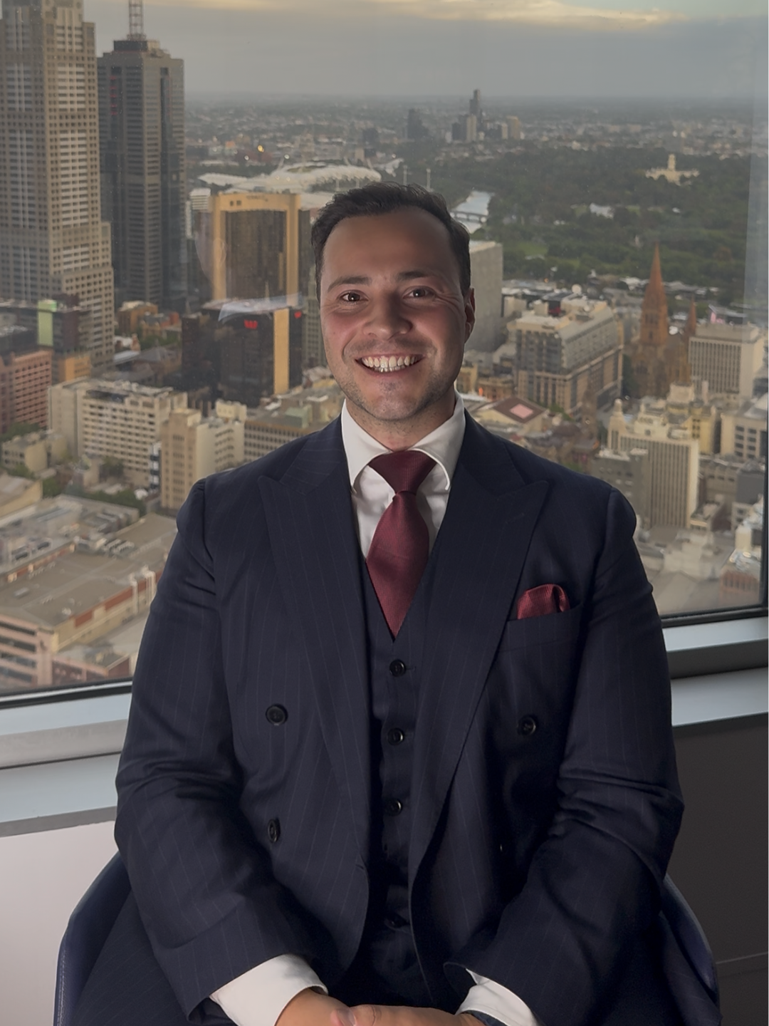 Professional headshot of a man in a suit with a white shirt and tie, smiling against a plain background.