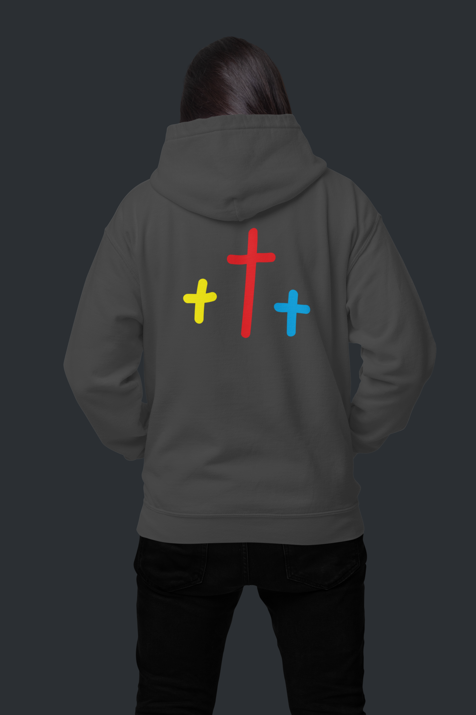 dark background back view of brunette woman wearing dark gray hoodie with three crosses yellow red and blue centered on back