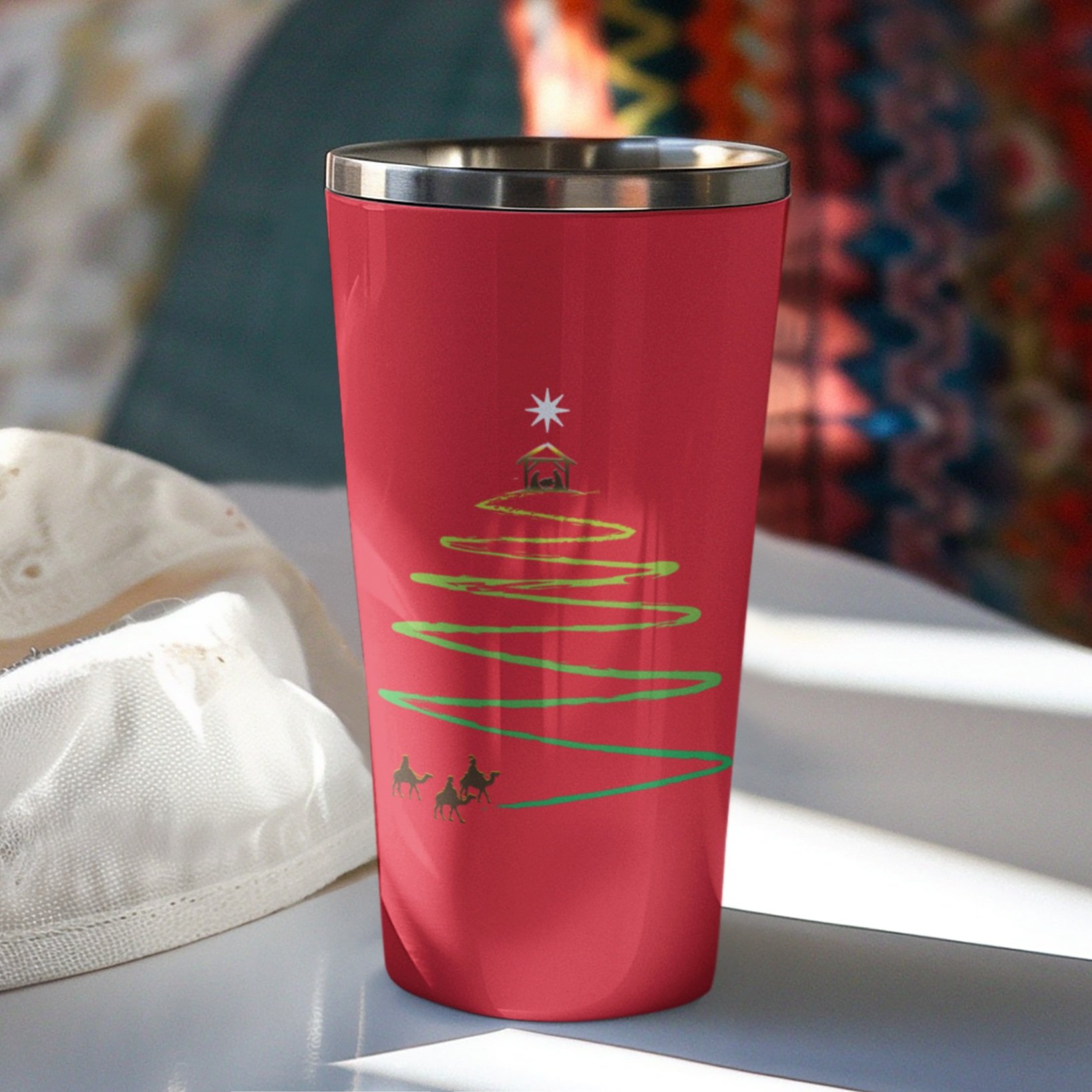 table with fabric and bright colors with red tumbler with image of wise men at bottom of green path that zigzags up shirt in shape of Christmas tree with nativity and star at top