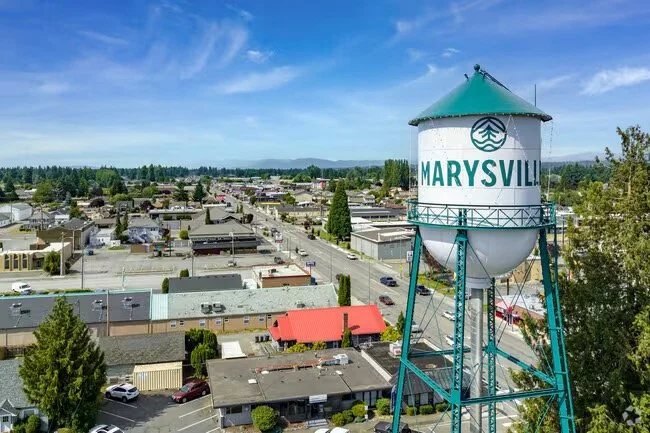 A water tower with the words 'Marysville' and a water park logo, overlooking a small town with commercial and residential buildings under a partly cloudy sky.