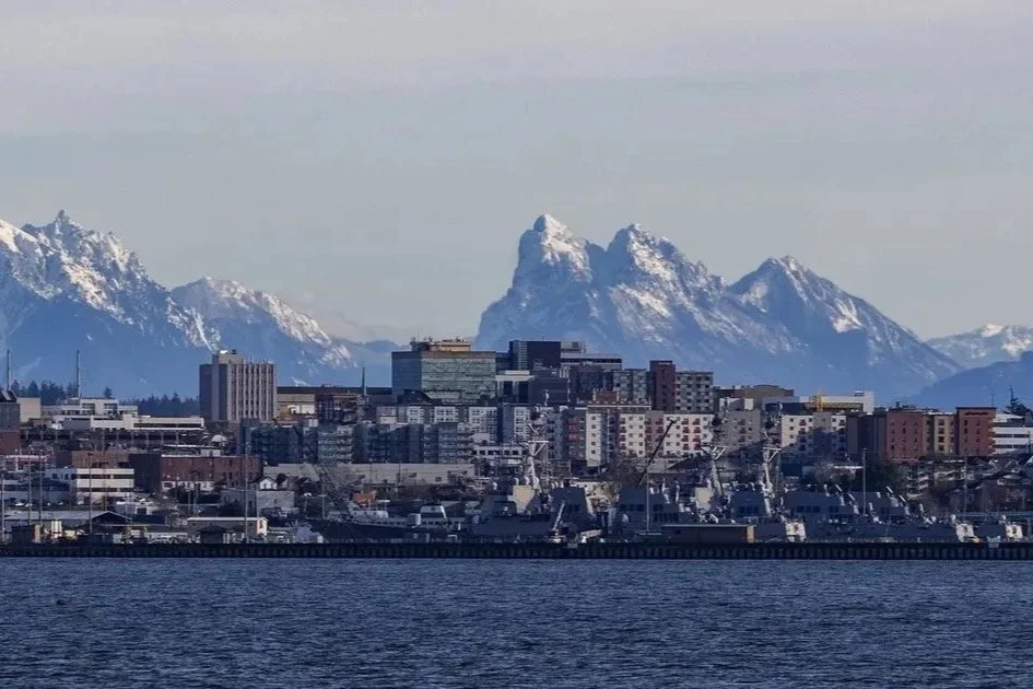 City skyline with buildings and boats in foreground, snow-capped mountains in background.