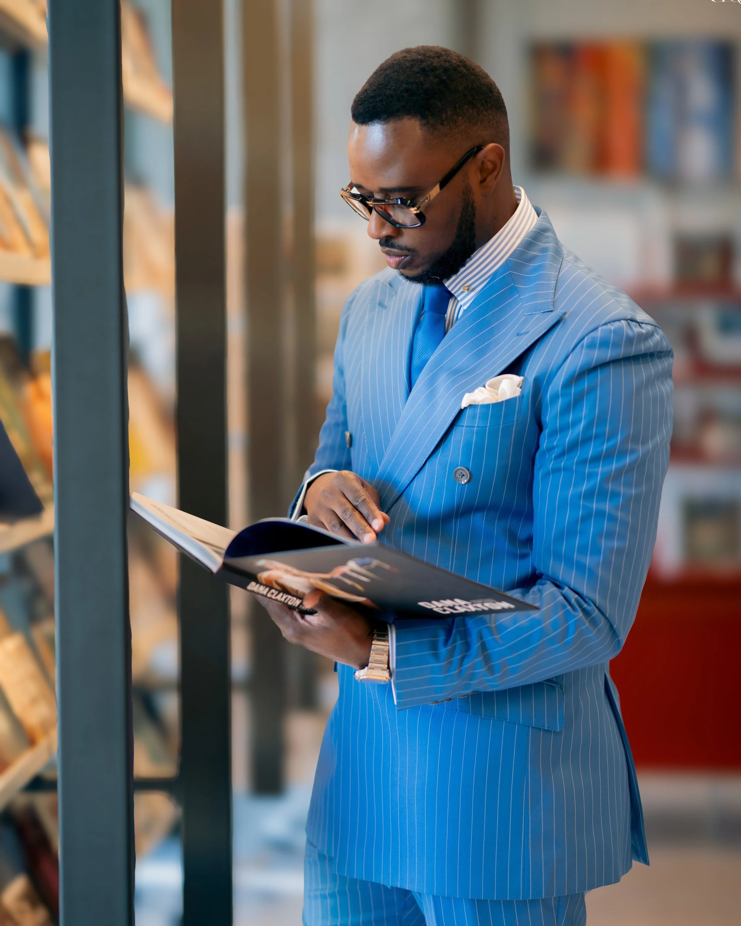 Raffiné Couture model wearing RC Blue Pinstripe a Double-Breasted Suit, reading a book