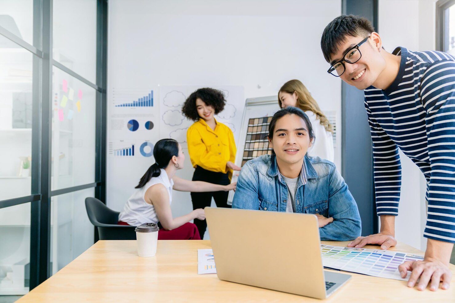 A group of diverse young professionals collaborating in a modern office, with a woman presenting color swatches and charts.