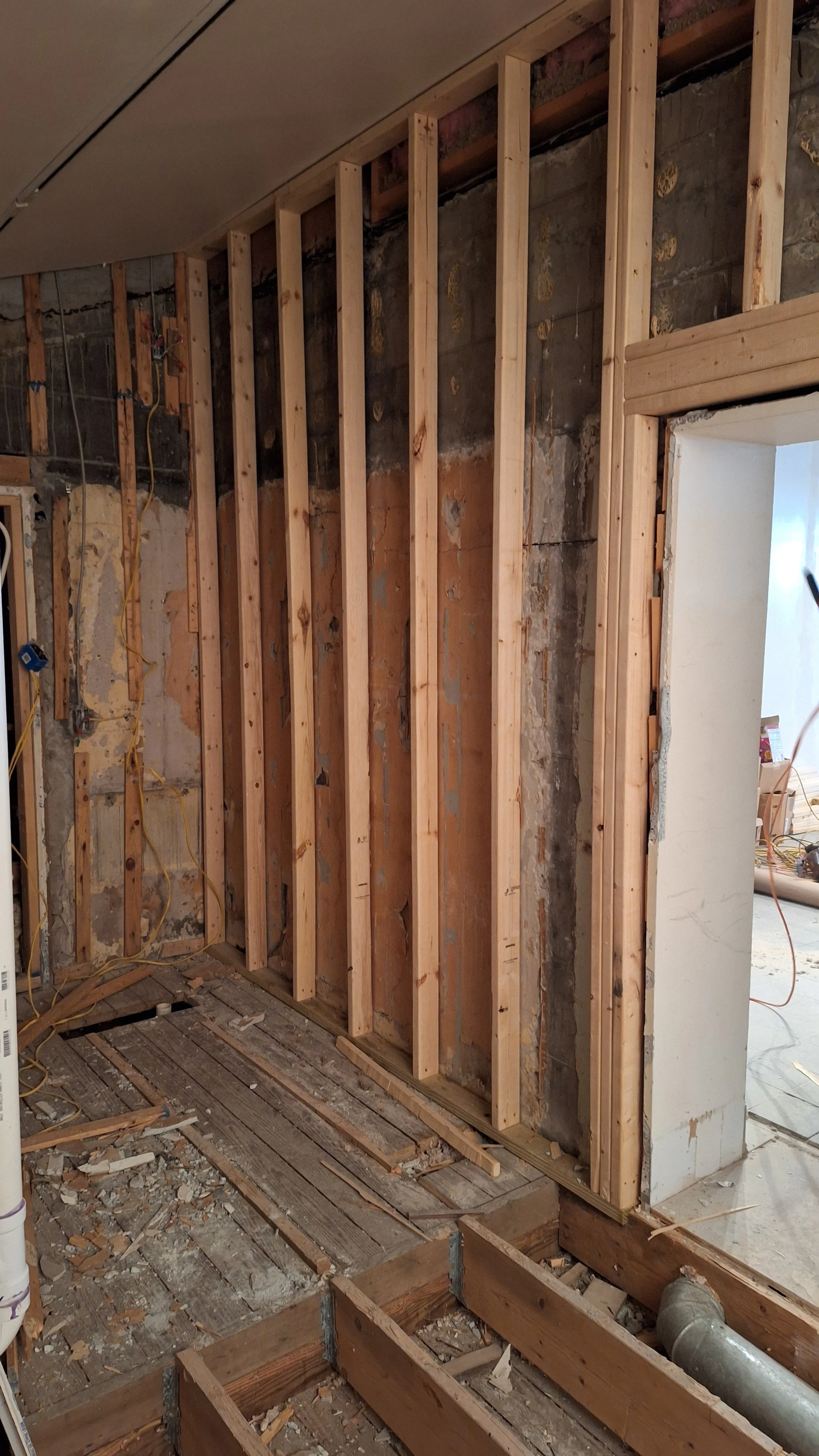 Interior construction site with exposed wooden framing, rough drywall, and scattered construction debris. Partial view of an unfinished wall and floor.