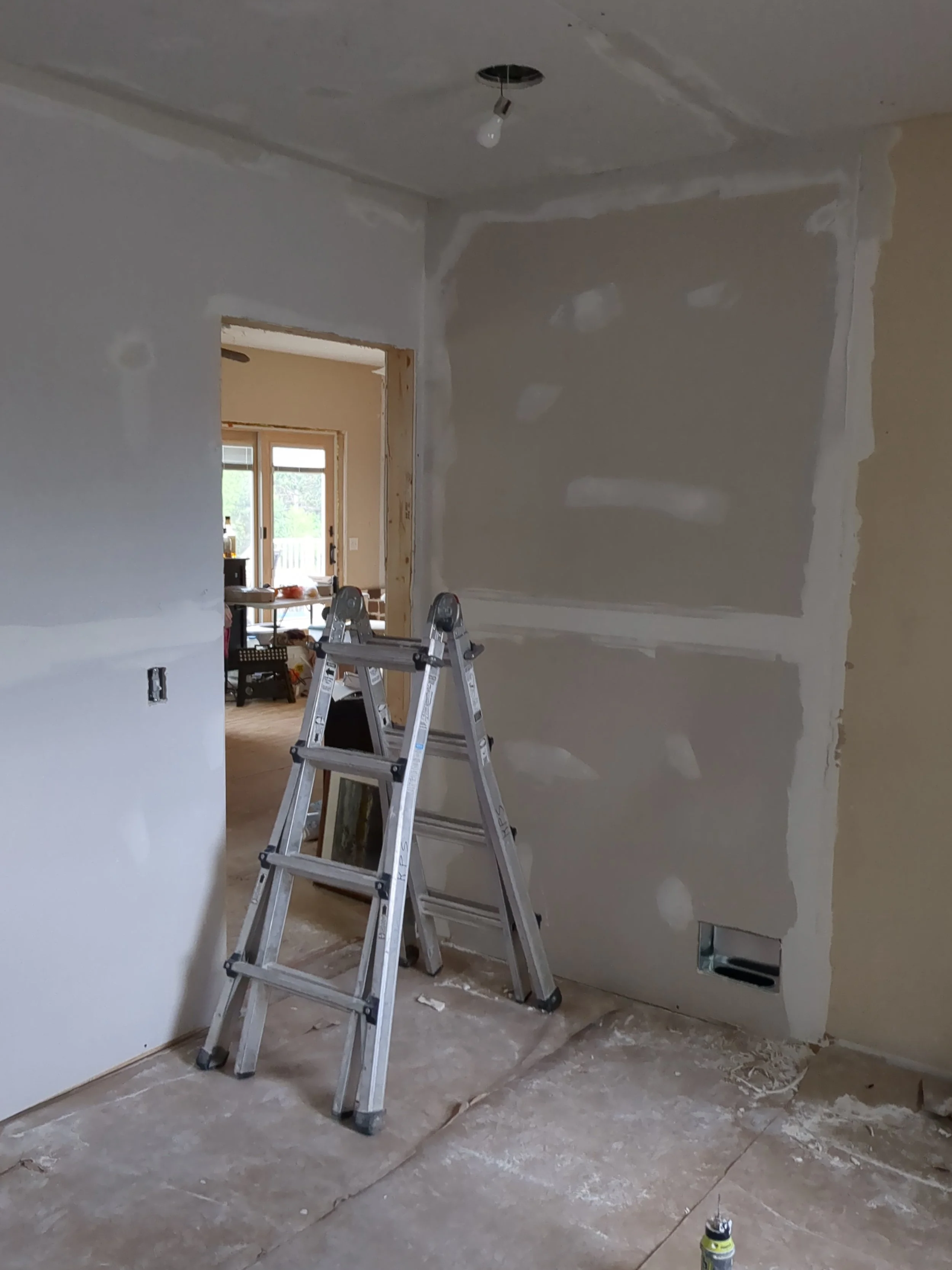 Interior room under renovation with drywall patches, a ladder, and exposed electrical outlet.