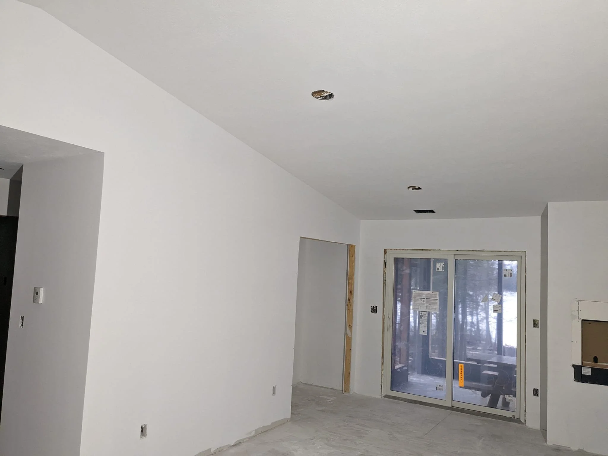 Unfinished interior room with white walls, sliding glass door, and ceiling lights during construction.