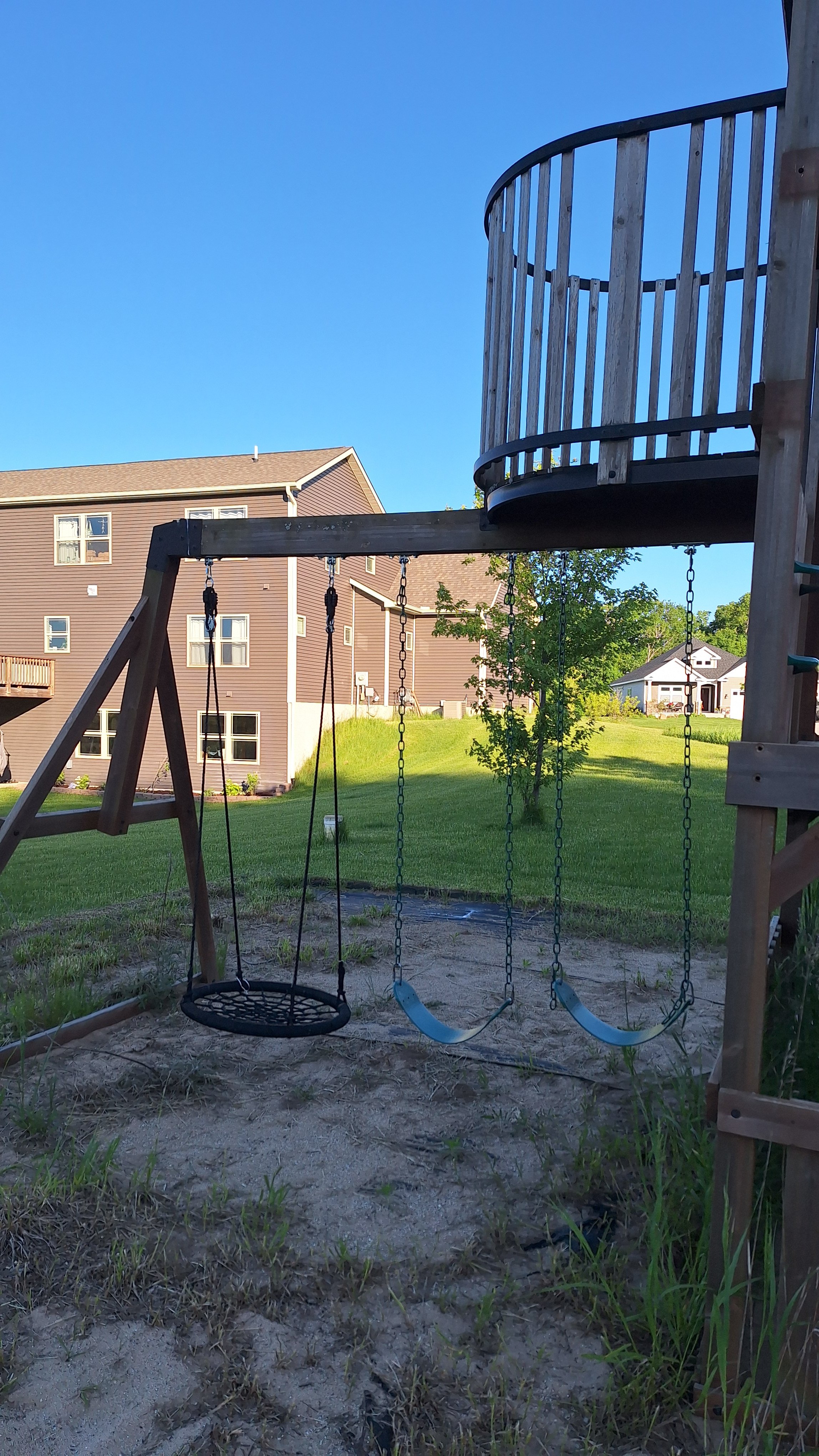 Corner of a building with beige siding, small window, garden with green bushes, and gravel ground covering.