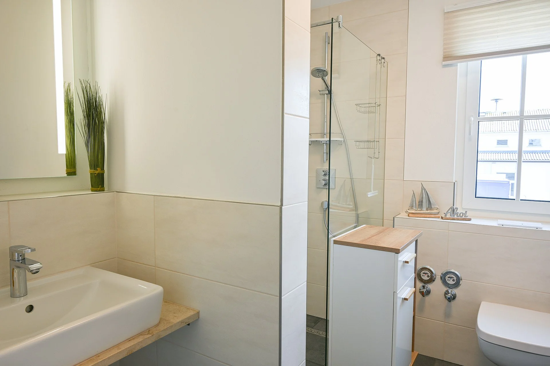 Ein Badezimmer mit Waschbecken, Dusche und WC, dekoriert mit einem kleinen Segelschiffmodell am Fenster.