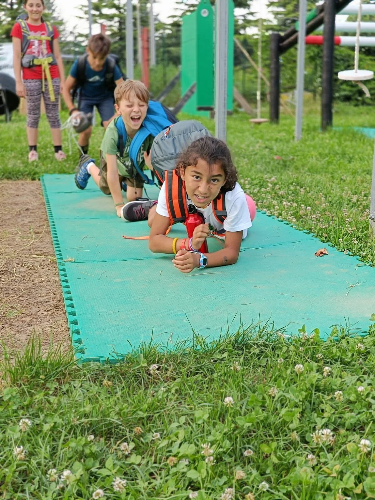 Bambini che si divertono in un parco avventura, strisciano su un tappetino verde.