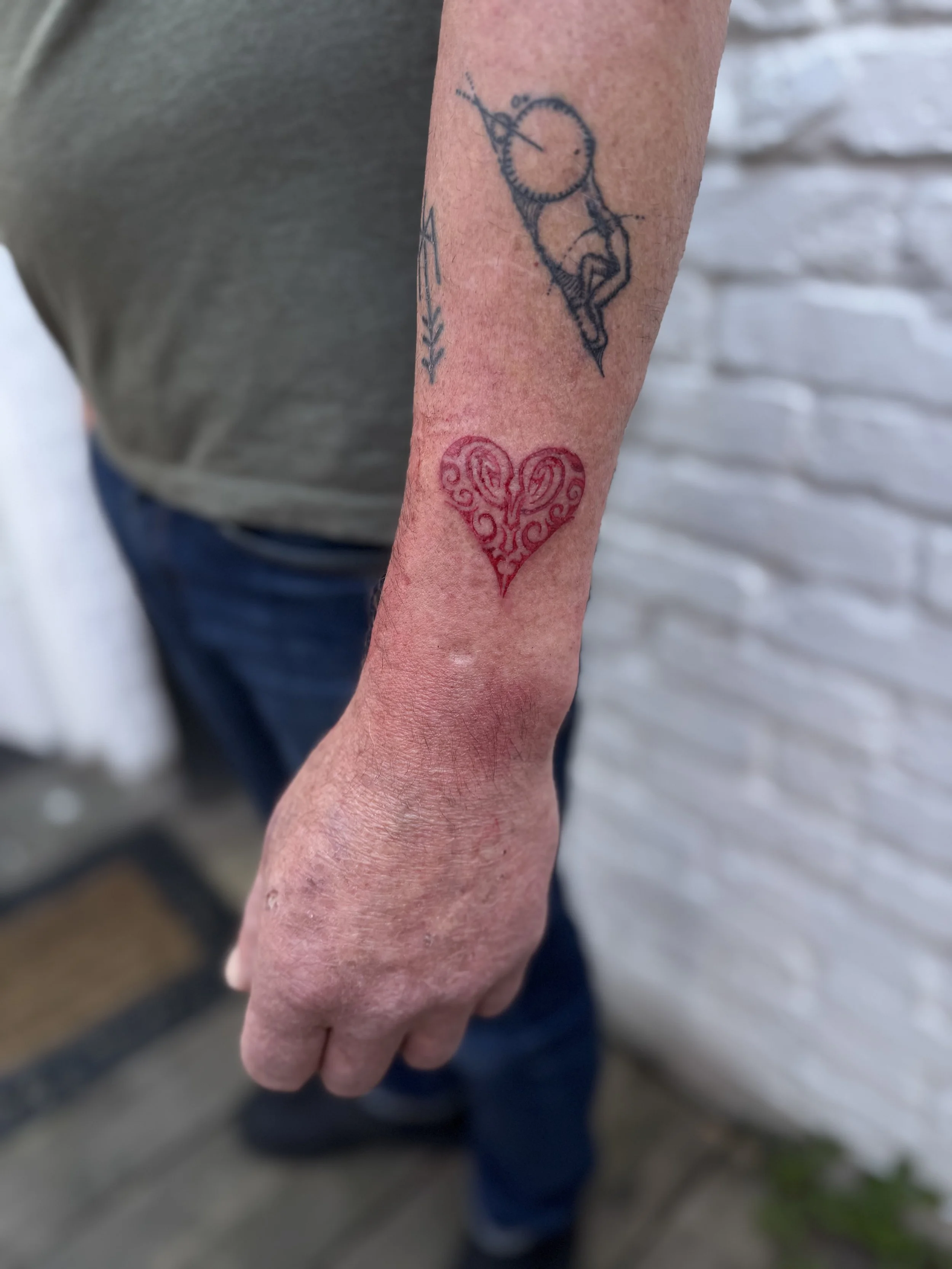 Tattoo of a heart with swirling patterns below a tattoo of a compass and a unicorn on a person's arm.