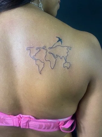 Tattoo of a world map in black ink on a person's upper back near the shoulder.