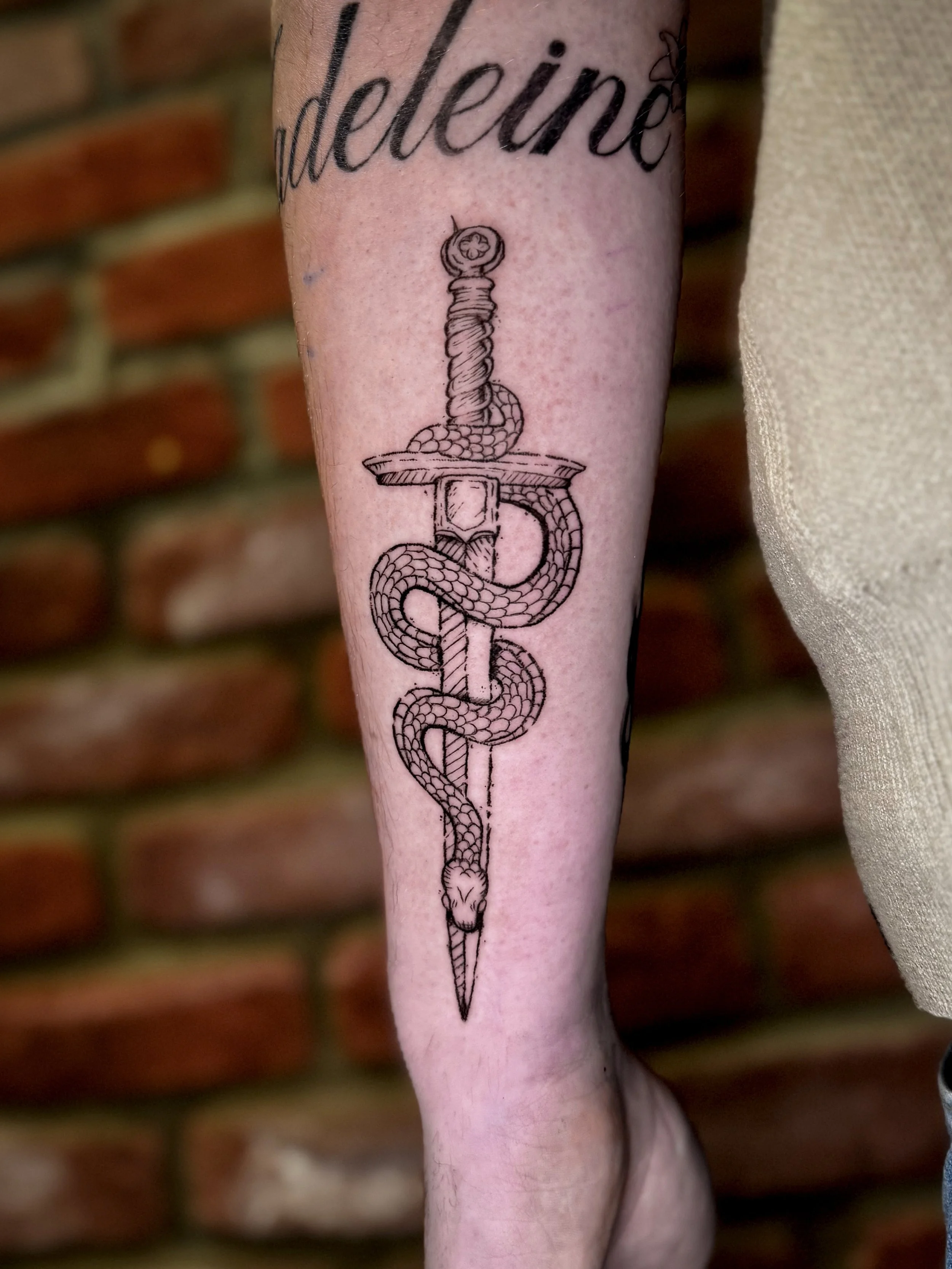 Tattoo of a black cat and a shadowy bat-like creature on a person's forearm against a green and yellow background.