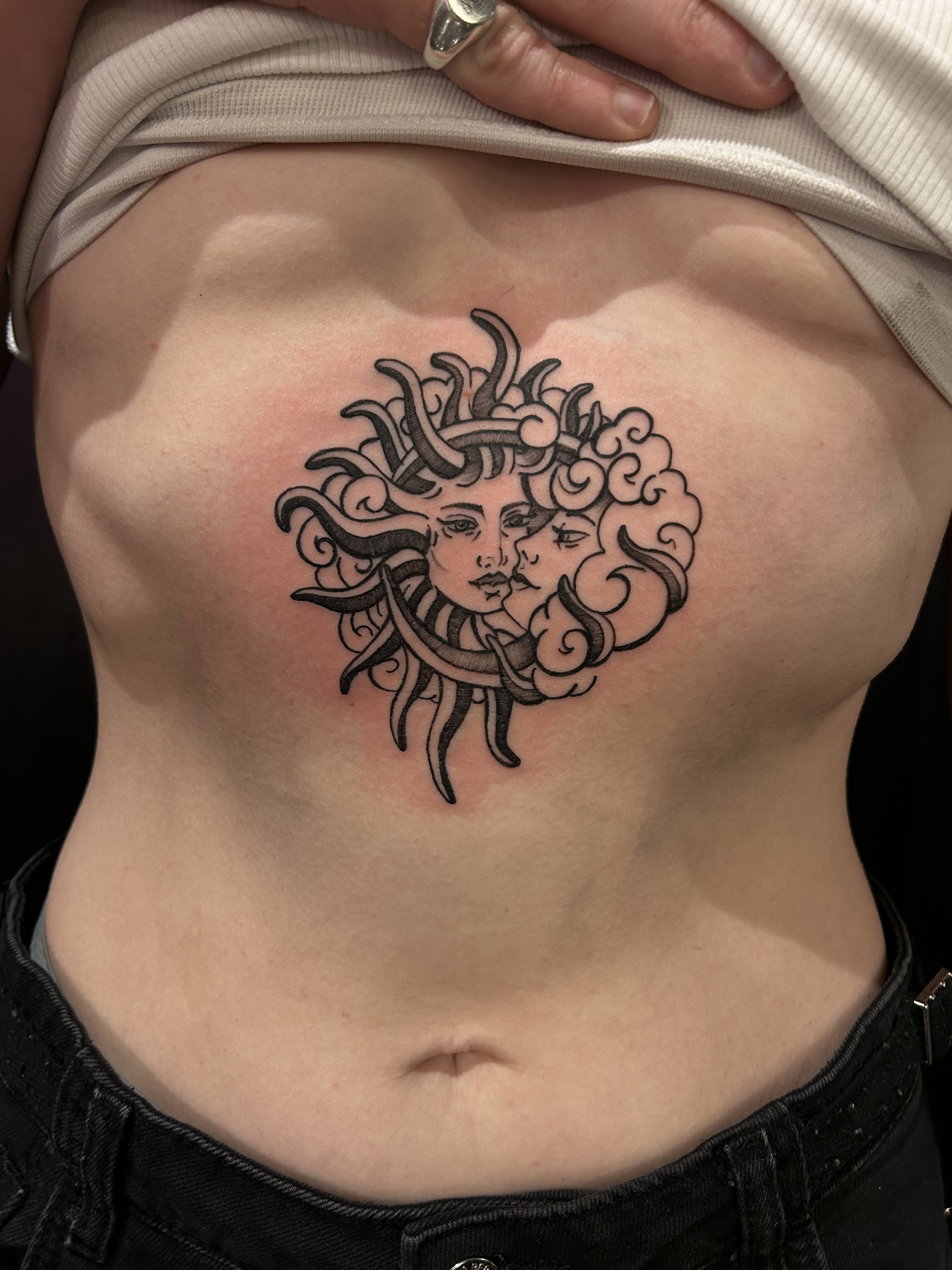 Tattoo of a face with flowing hair made of clouds and tentacles on a person's torso