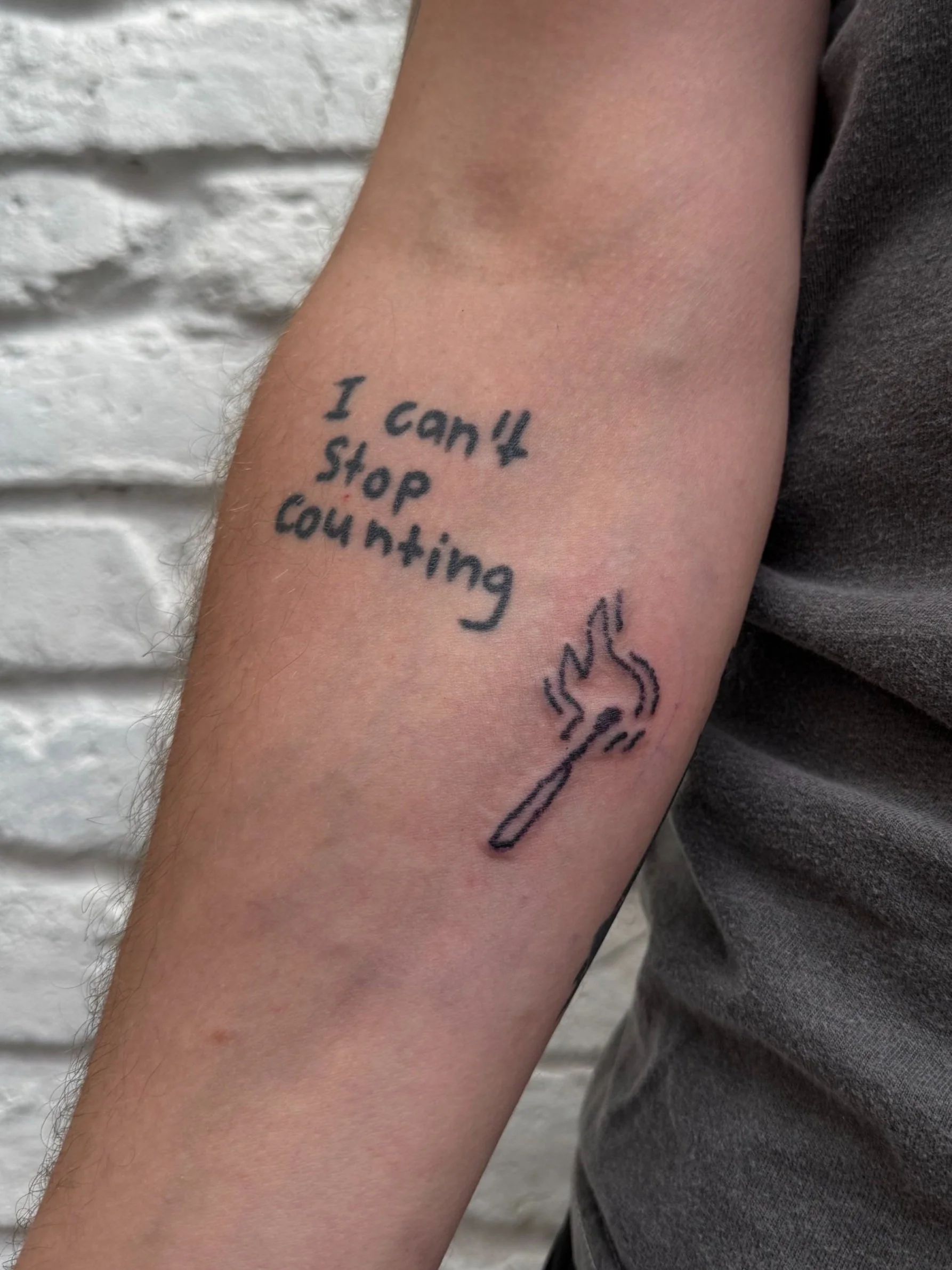 Tattoo on person's arm with the words 'I can't stop counting' and a drawing of a lit matchstick.