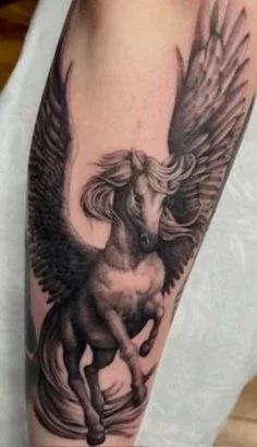 Tattoo of a cartoon-style samurai with a smiling face, wearing a traditional helmet, holding a sword, and dressed in armor on the upper arm. Another smaller tattoo of a cartoonish face with sharp teeth and a tongue sticking out is on the lower arm.