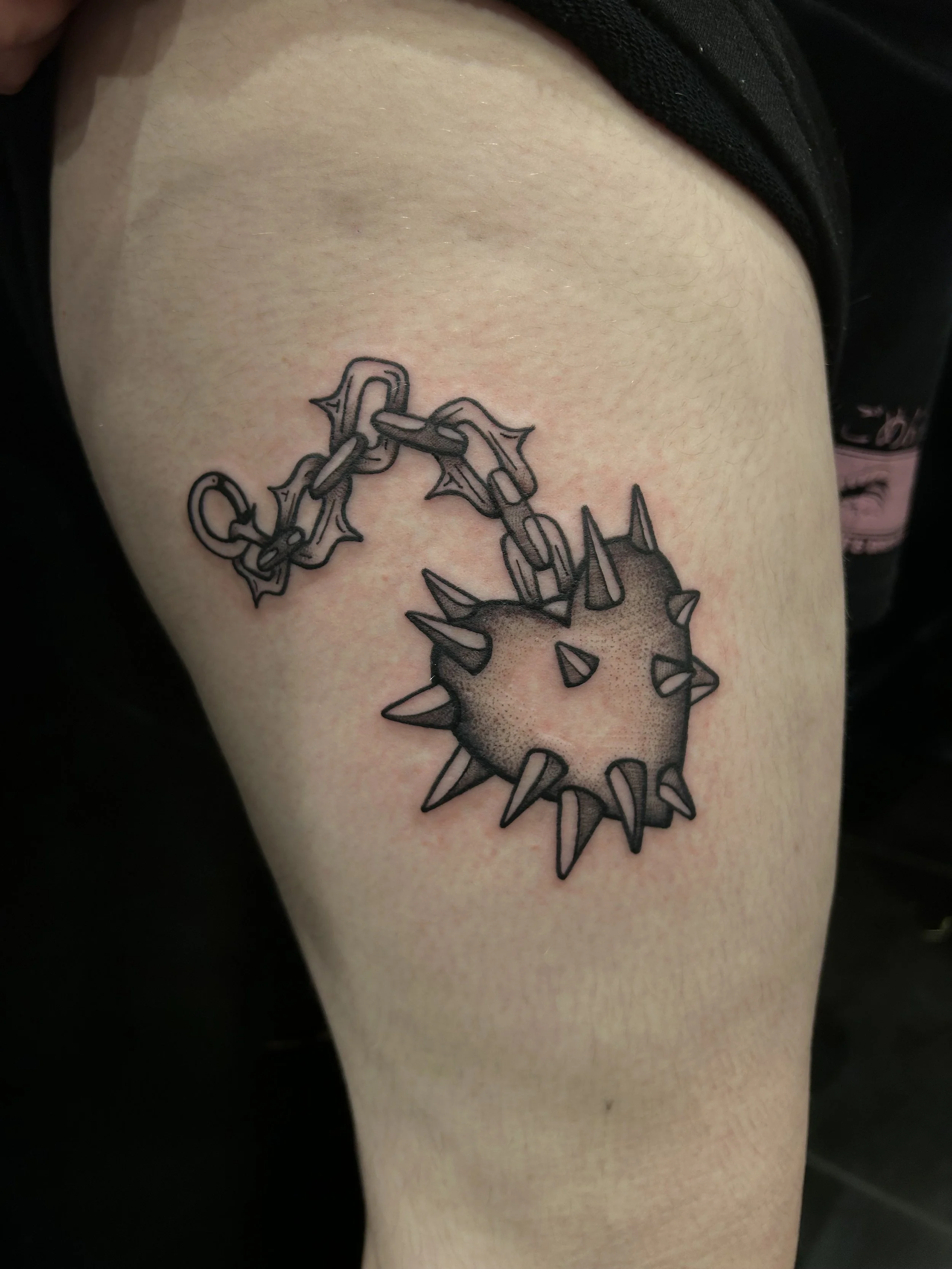 Tattoo of a spiked ball and chain on person's thigh.
