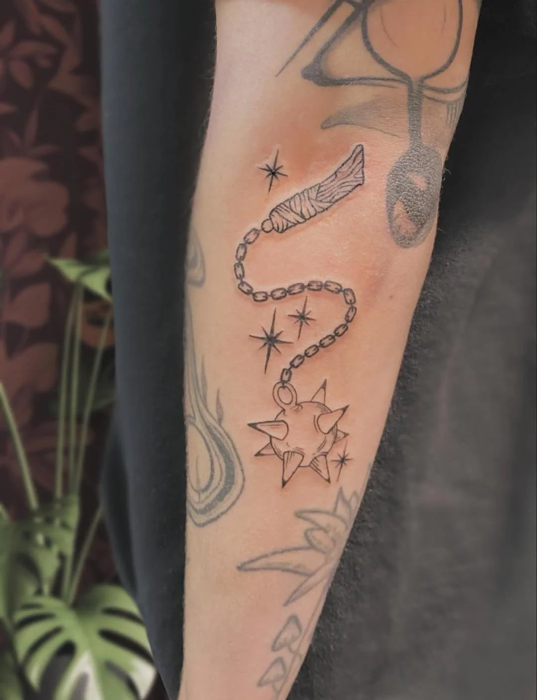 Tattoo of a shuriken with spikes, surrounded by stars, attached to a chain with beads, on a person's arm.