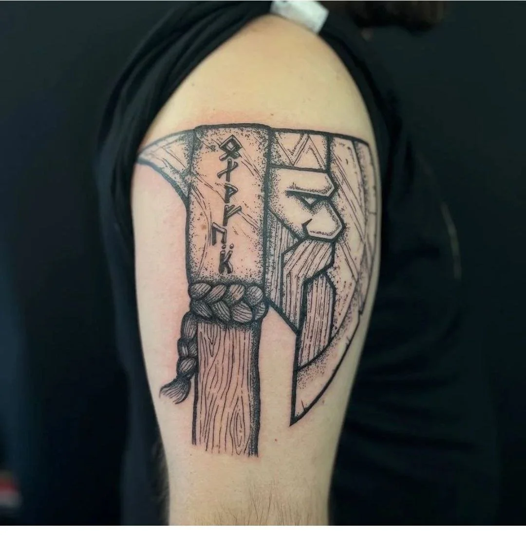 Tattoo of a Viking warrior's profile with a helmet, beard, and braided hair, with runic characters on the armor.