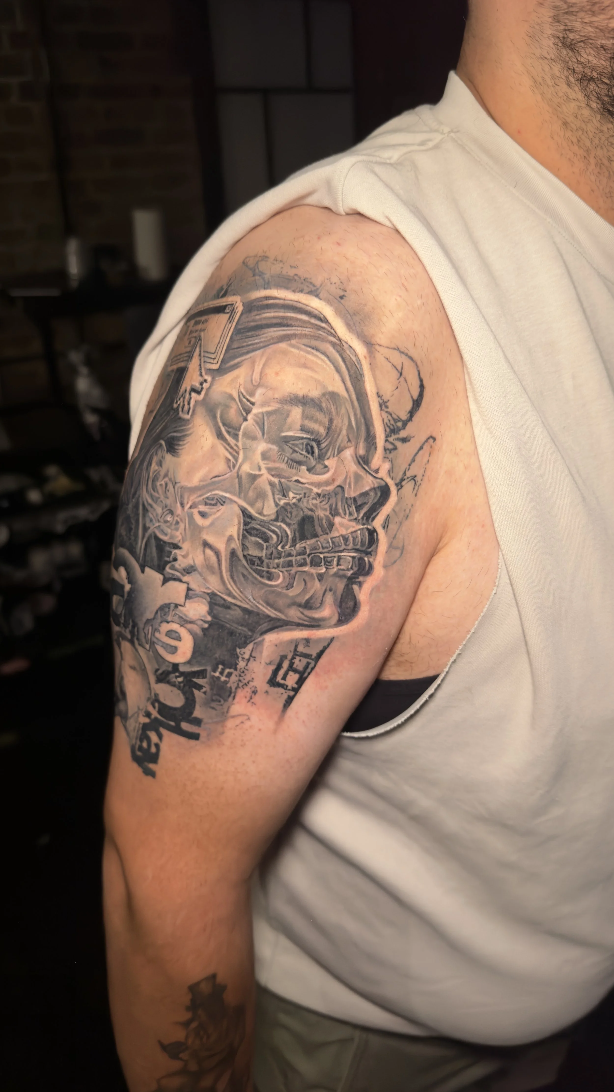 A person's forearm with a small tattoo of two puzzle piece outlines in black ink, set against a white brick wall background.