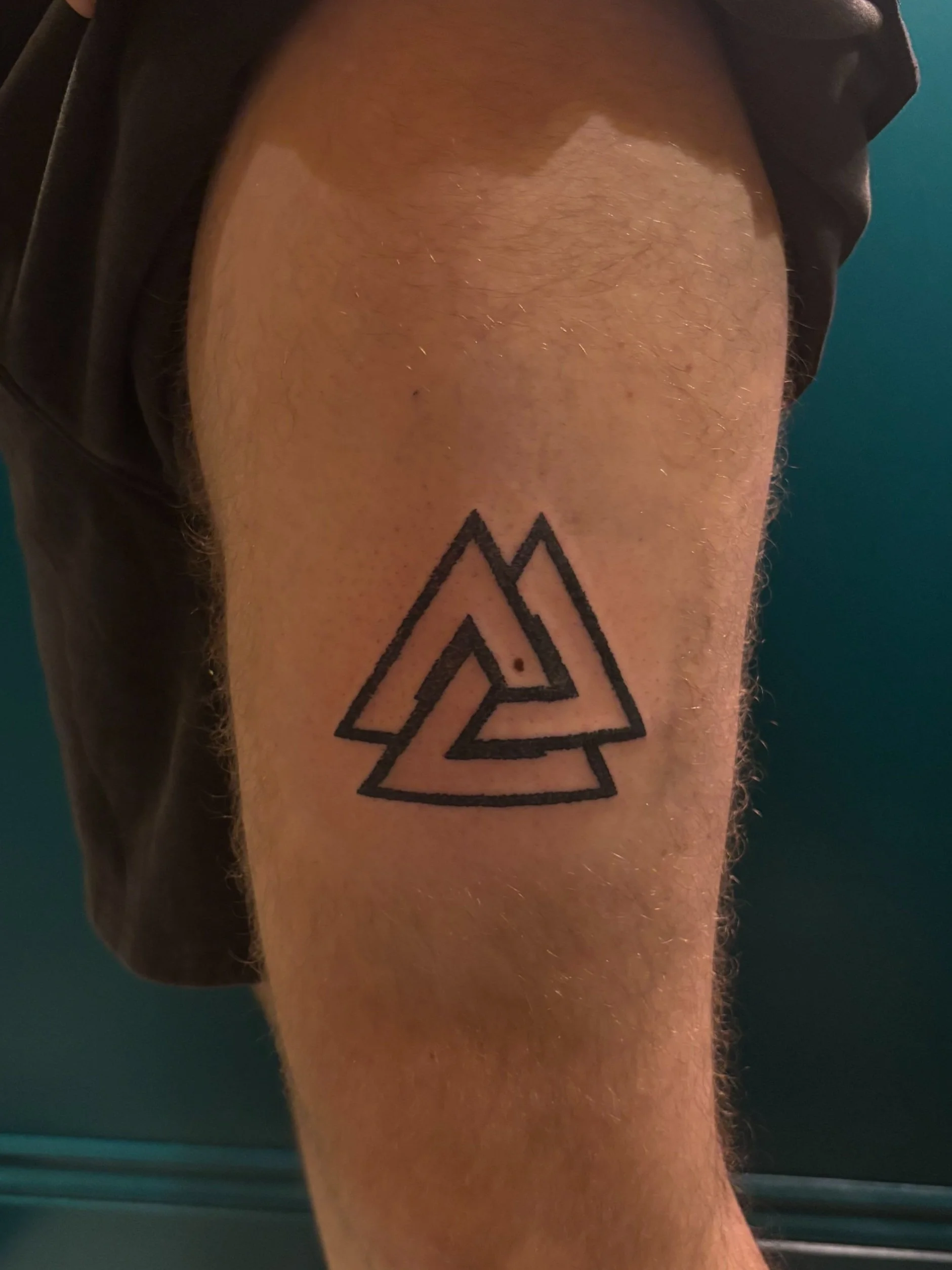 A tattoo of the Valknut symbol on a person's upper leg.