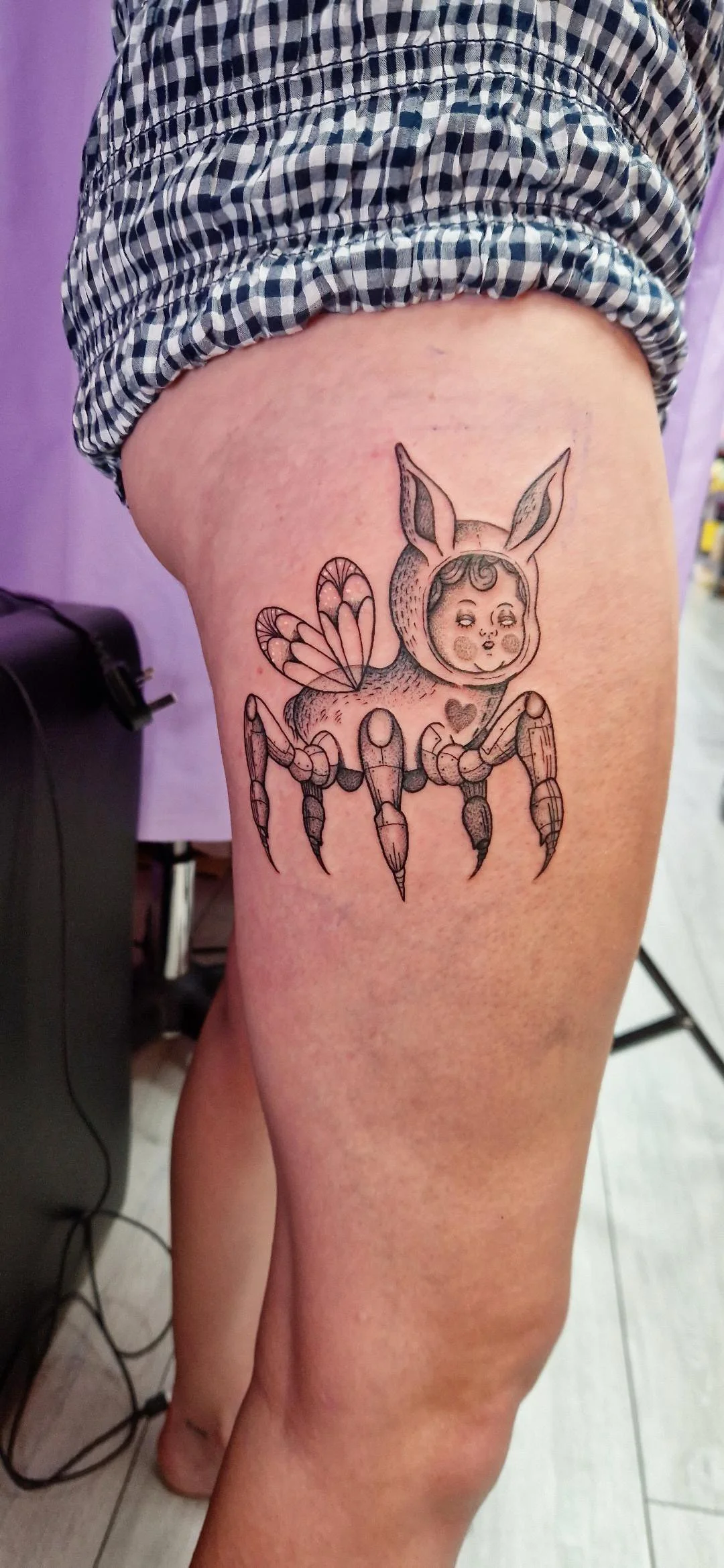 Tattoo of a cute hybrid creature with a butterfly wings, bunny ears, and a human face on the thigh.