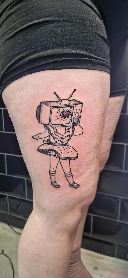 Tattoo of a girl with a TV as a head, wearing a dress and shoes, on a person's thigh.