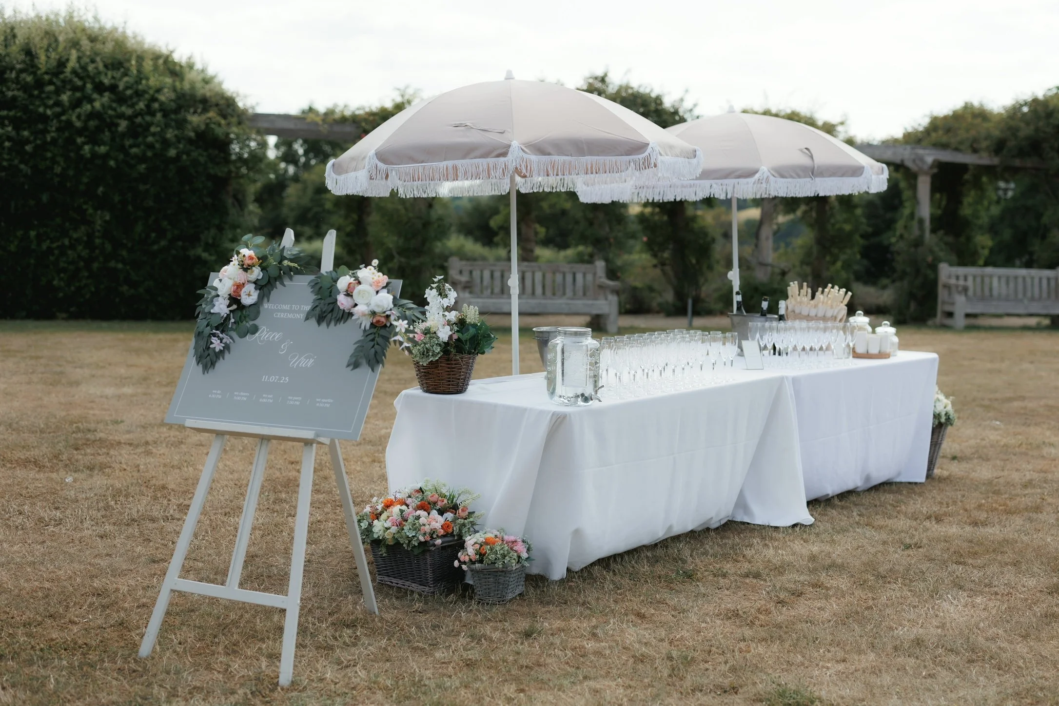 Welcomes drinks table with parasouls and a welcome sign on an easle. Bottles of prosecco and champagne rest in ice buckets waiting to be poured. At Euridge Manor