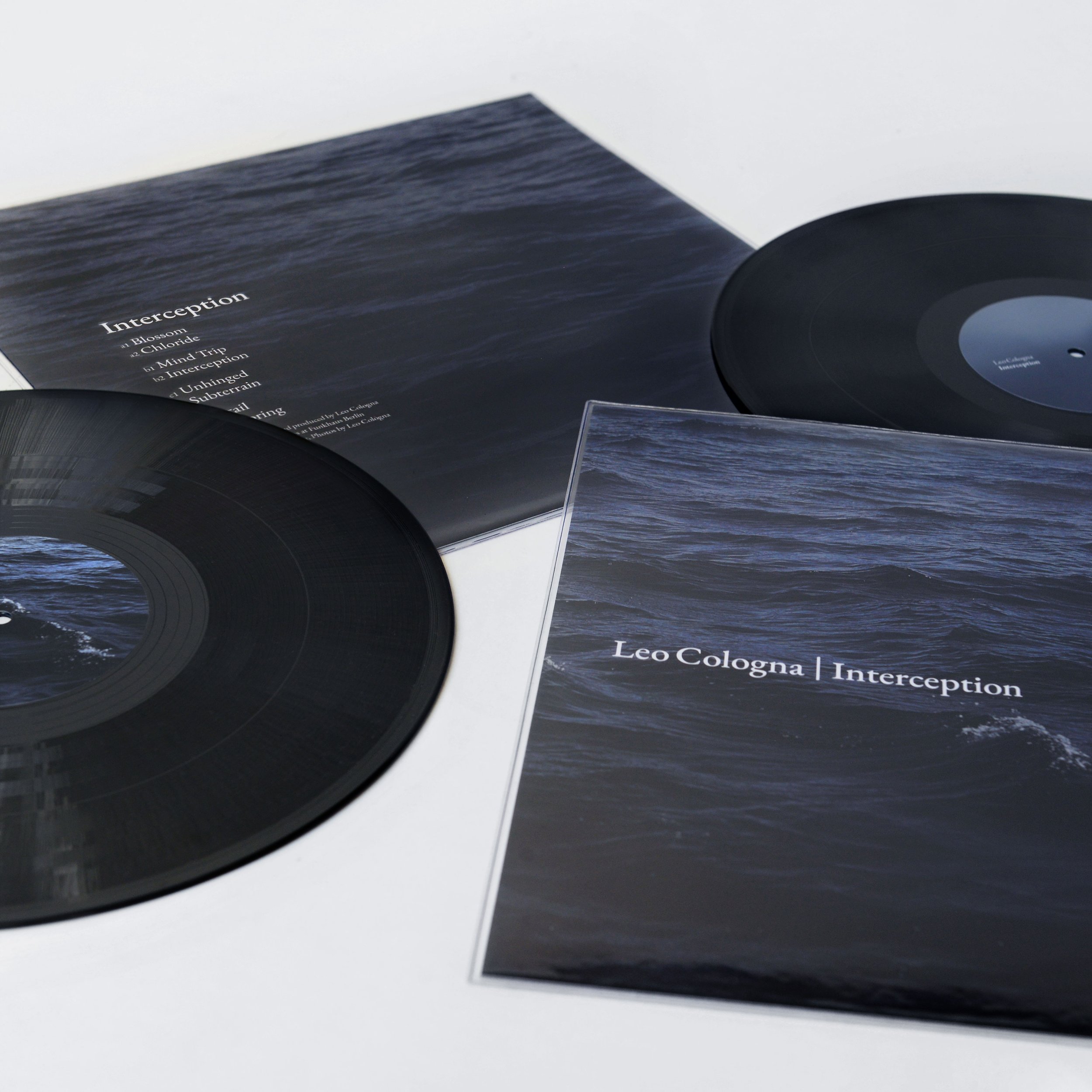 Close-up image of a vinyl record and its album cover with a dark, ocean-like background and white text listing songs, including 'Interception', 'Blossom', and 'Mind Trip'.