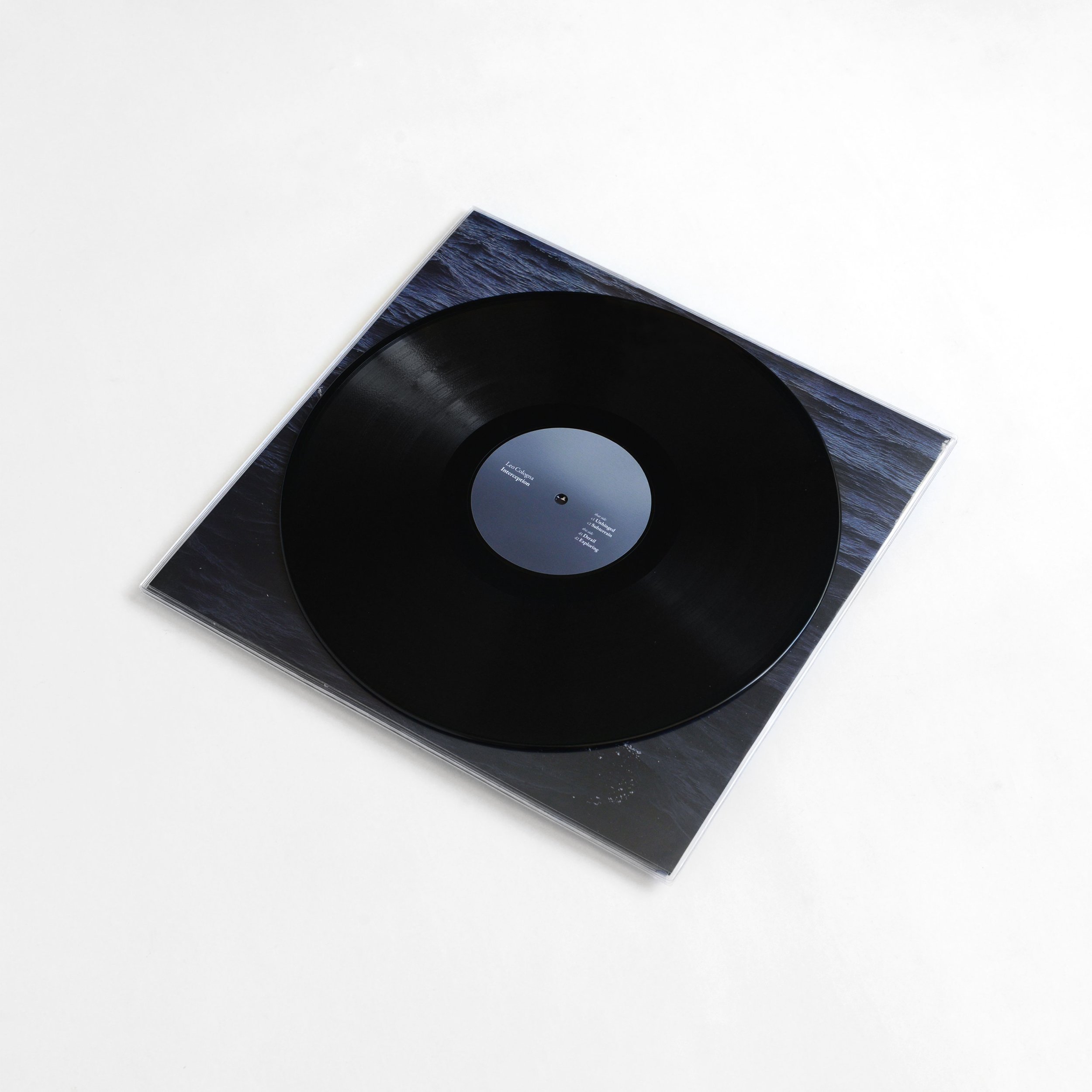 A black vinyl record in its paper sleeve, partially visible, placed on a white surface.
