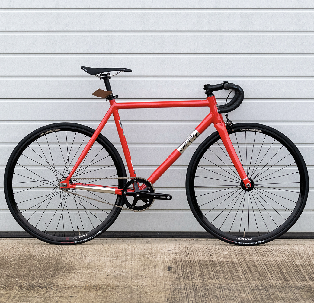 Red road bicycle with black wheels and handlebar, set against a white garage door.