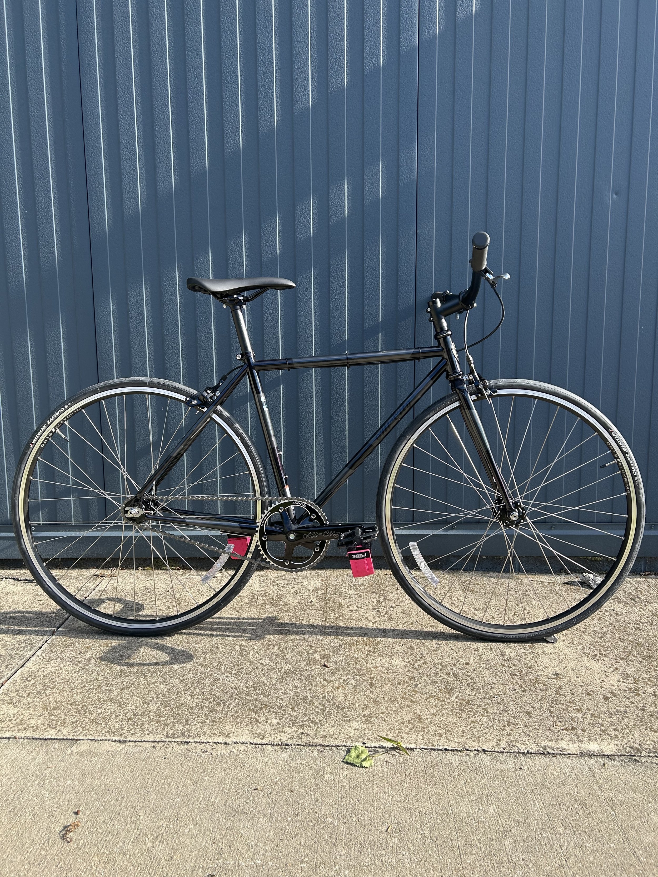 A black bicycle leaning against a blue textured wall with vertical ridges.