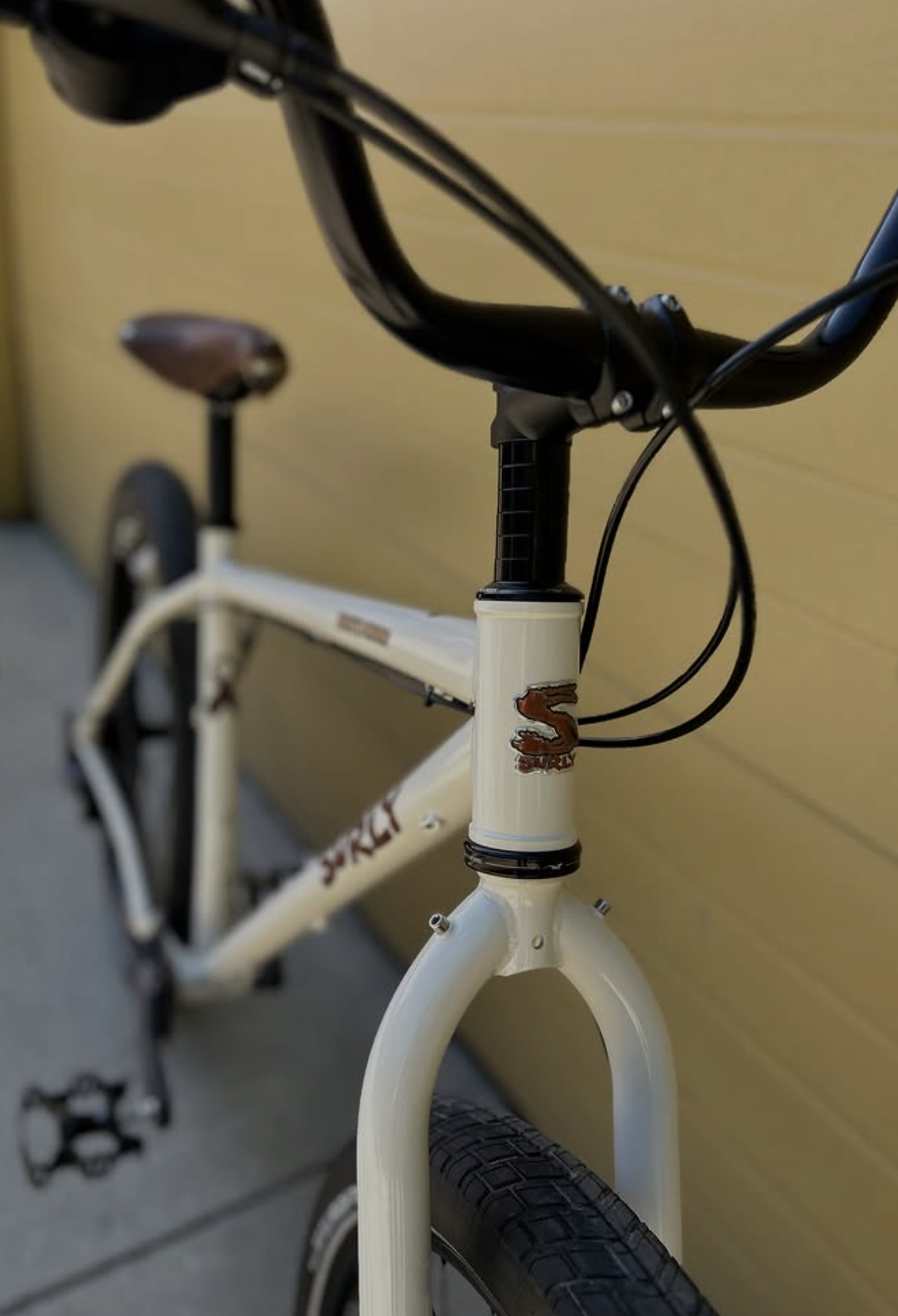 A close-up of a white BMX bicycle with black handlebars and black tires, leaning against a yellow wall.
