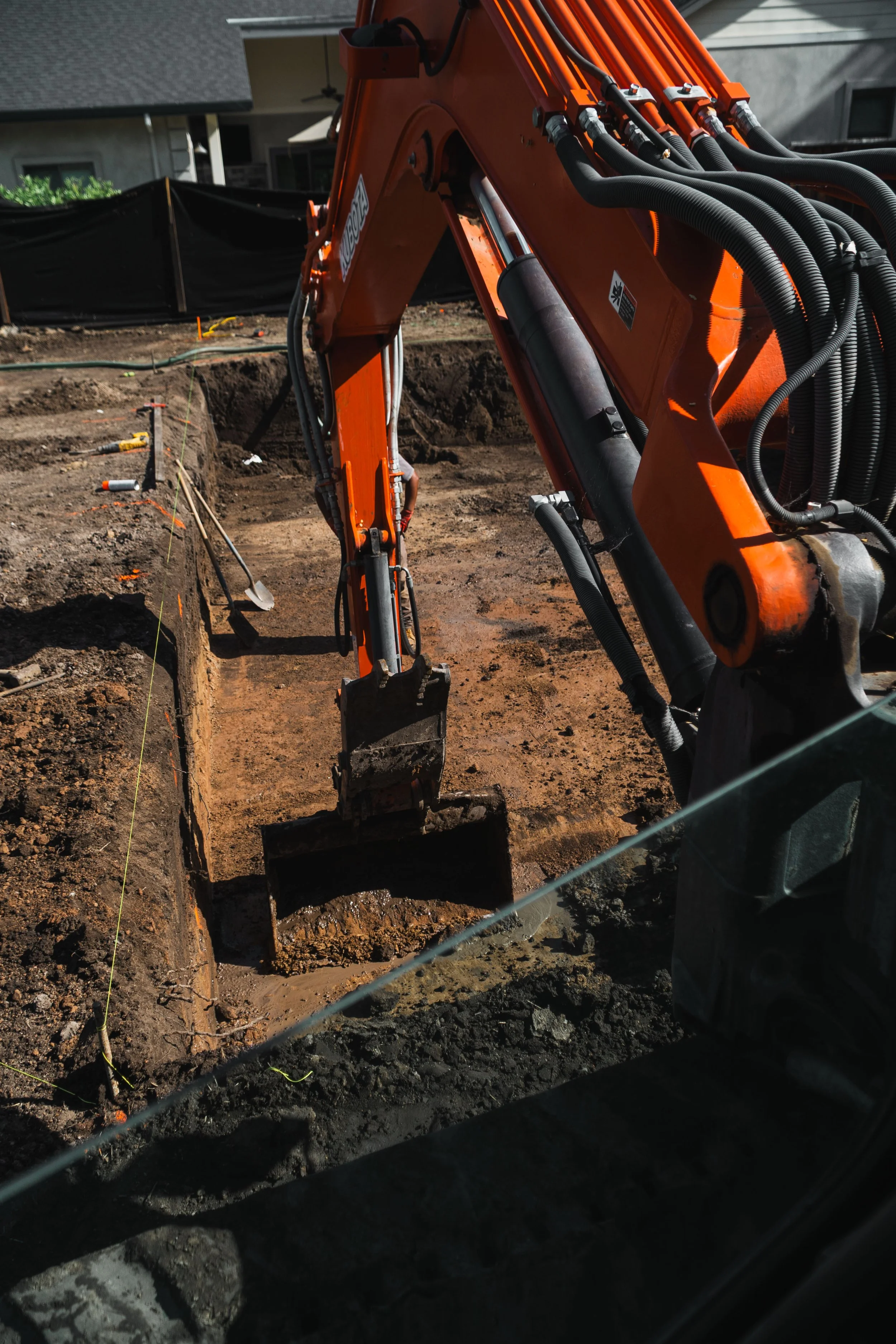 Construction site with an orange excavator digging a trench in dirt, with construction tools and safety markings visible.