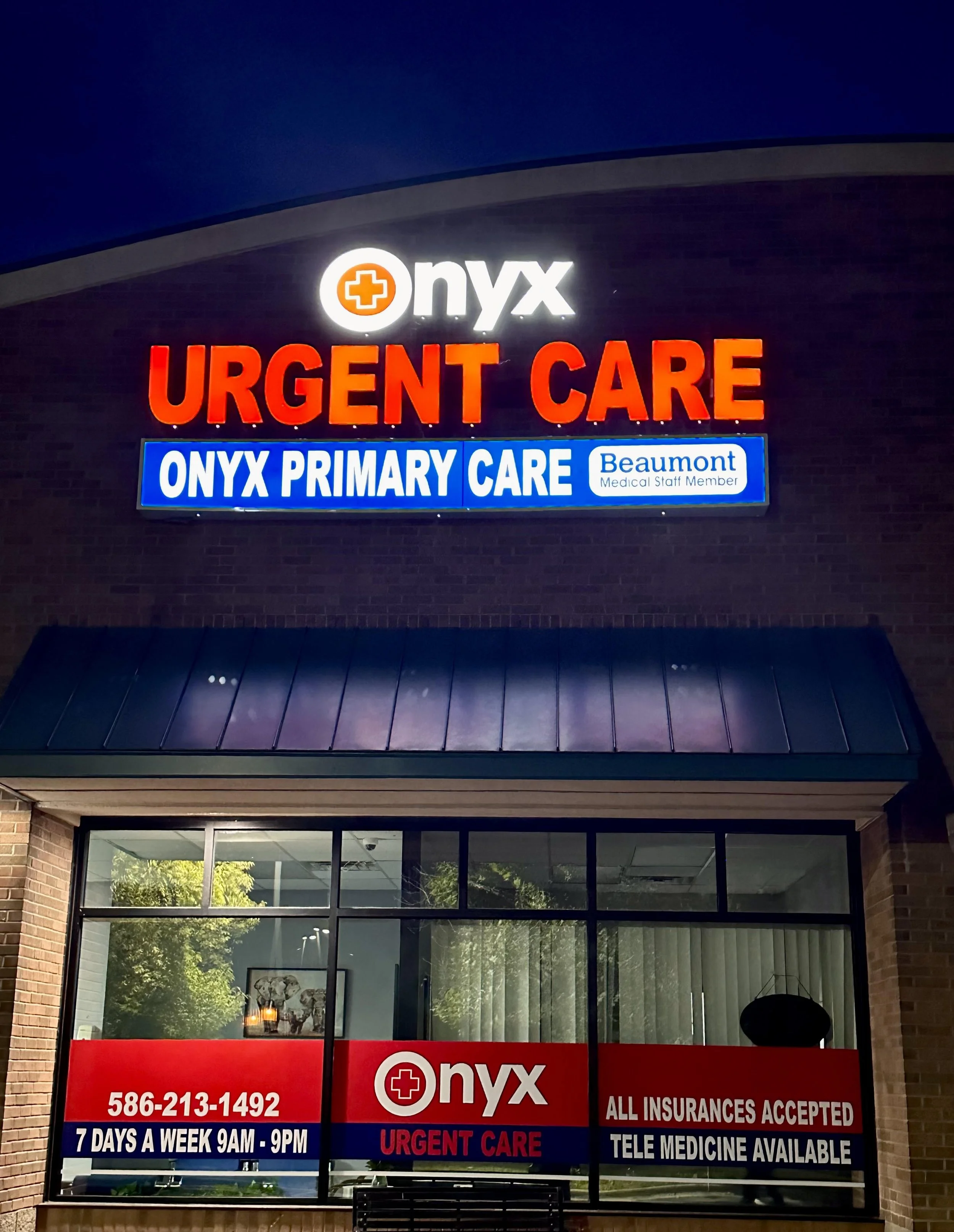Exterior of Onyx Urgent Care and Primary Care clinic at night, with illuminated signs displaying the clinic's name, contact number, hours, and services, including insurance and telemedicine.