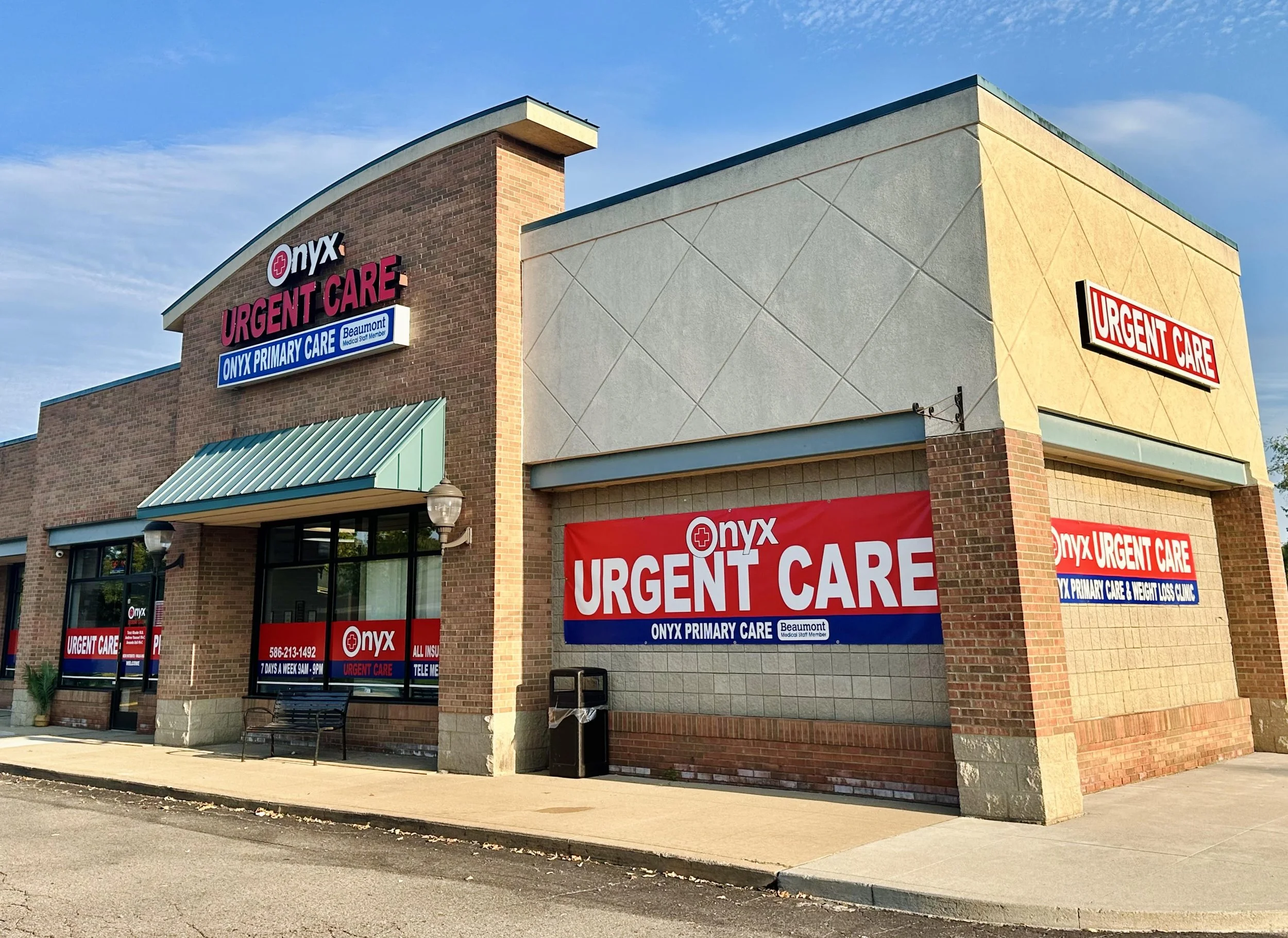 Exterior view of an urgent care medical clinic with signs reading "Onyx Urgent Care" and "Onyx Primary Care" in a shopping center, blue sky above.