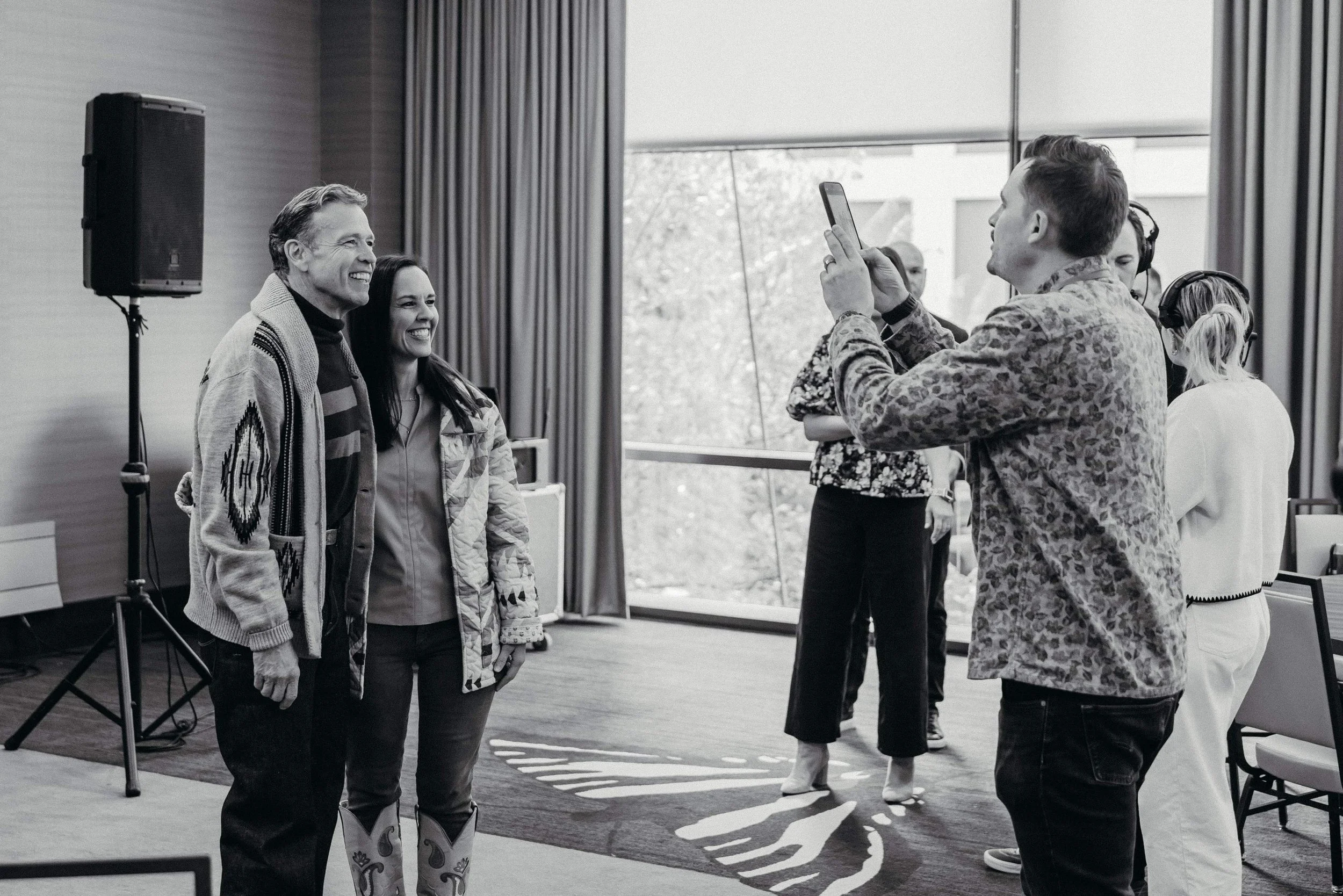 Katie Weiss and Donald Miller are taking a photo indoors, with a large window and curtains in the background.